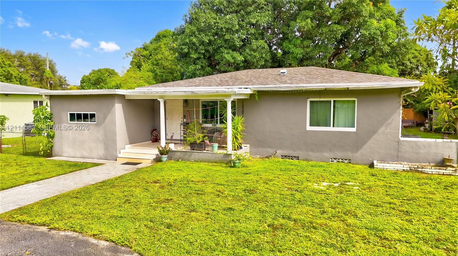 13301 NW Miami Court, Miami, FL 33168 Single-story residence featuring a gray stucco exterior, a covered entryway with structural columns, and a paved walkway