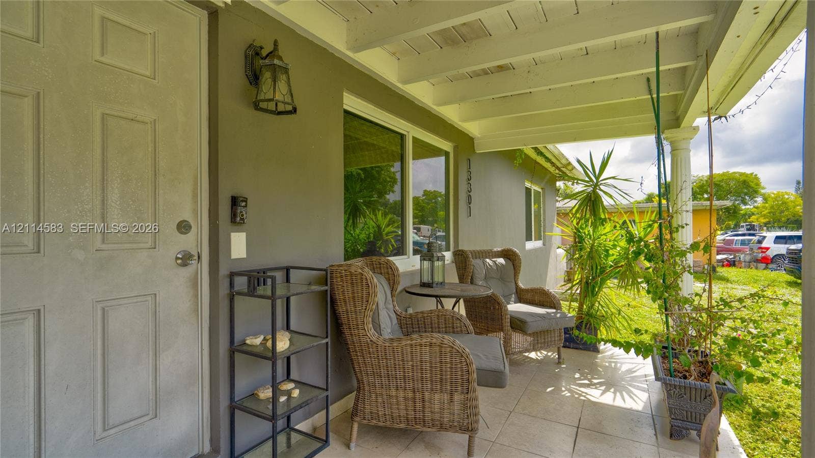 13301 NW Miami Court, Miami, FL 33168 Covered front porch featuring tile flooring, exposed beam ceiling, decorative column, and wall-mounted exterior lighting