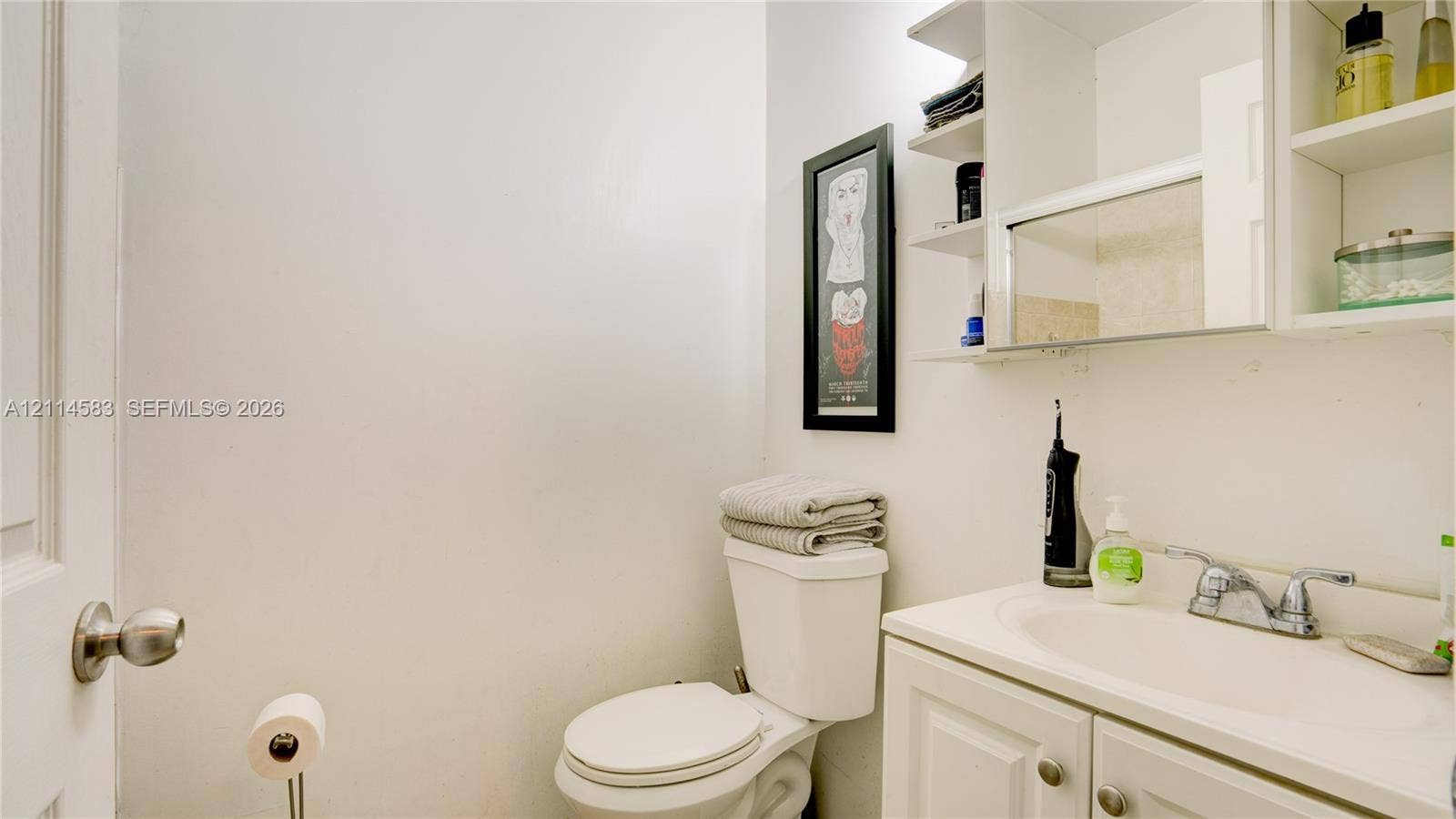 13301 NW Miami Court, Miami, FL 33168 White vanity cabinet featuring an integrated sink, polished chrome dual-handle faucet, and overhead cabinetry with built-in shelving and mirror