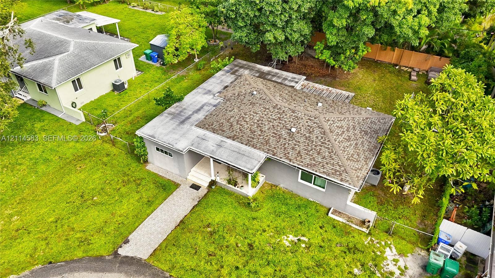 13301 NW Miami Court, Miami, FL 33168 Aerial perspective of a single-story residence featuring a shingled roof, a paved walkway, a concrete-surfaced entryway, and an expansive yard with mature trees
