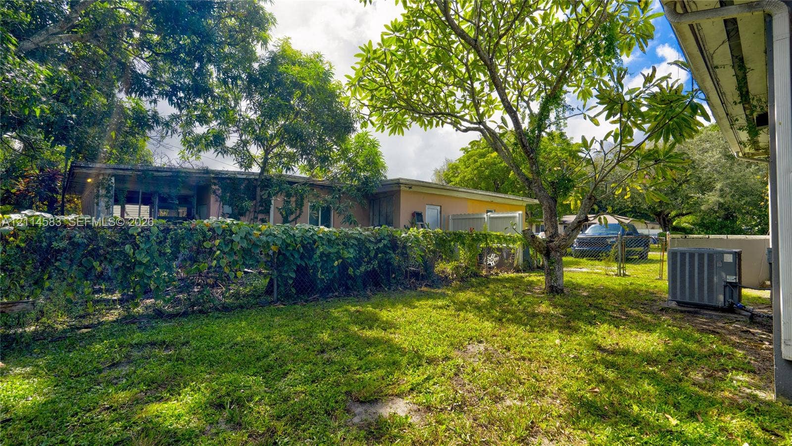 13301 NW Miami Court, Miami, FL 33168 Exterior grounds featuring a spacious lawn, mature trees, a chain-link fence, and an exterior HVAC unit