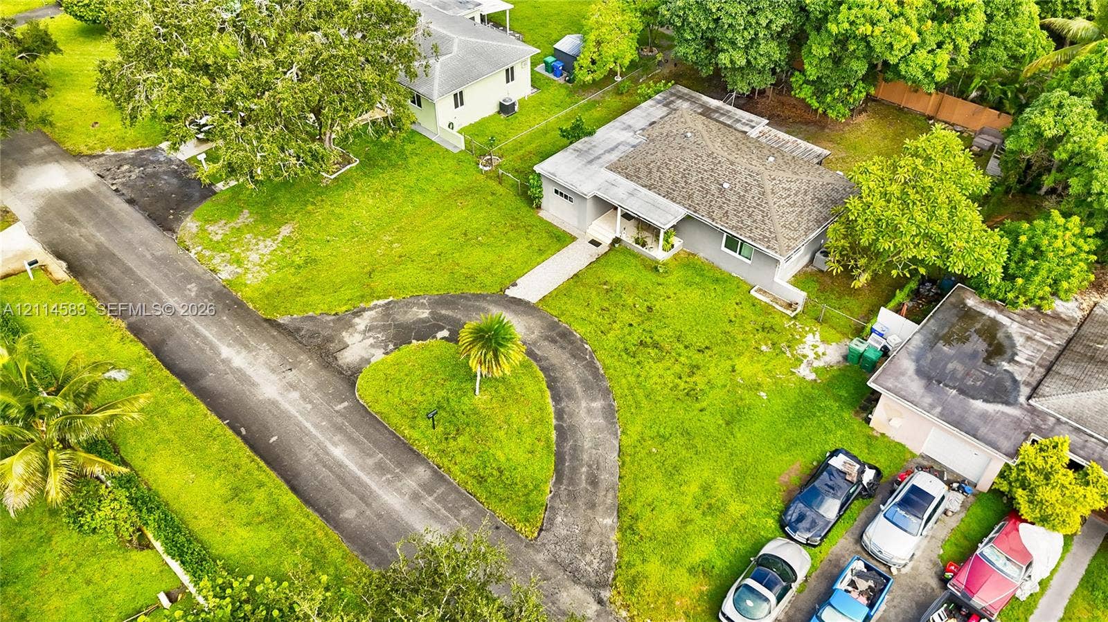13301 NW Miami Court, Miami, FL 33168 Aerial perspective of a single-story residence featuring a hipped roof, attached garage, paved circular driveway, and established landscaping