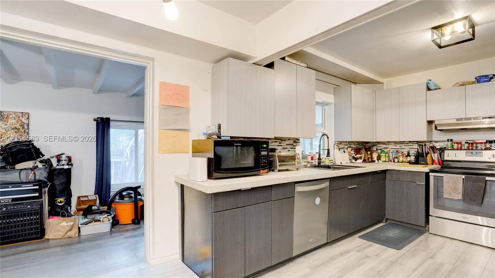 13301 NW Miami Court, Miami, FL 33168 Kitchen featuring two-tone flat-panel cabinetry, light-toned stone-finish countertops, multi-colored linear tile backsplash, stainless steel dishwasher, and wood-finish flooring