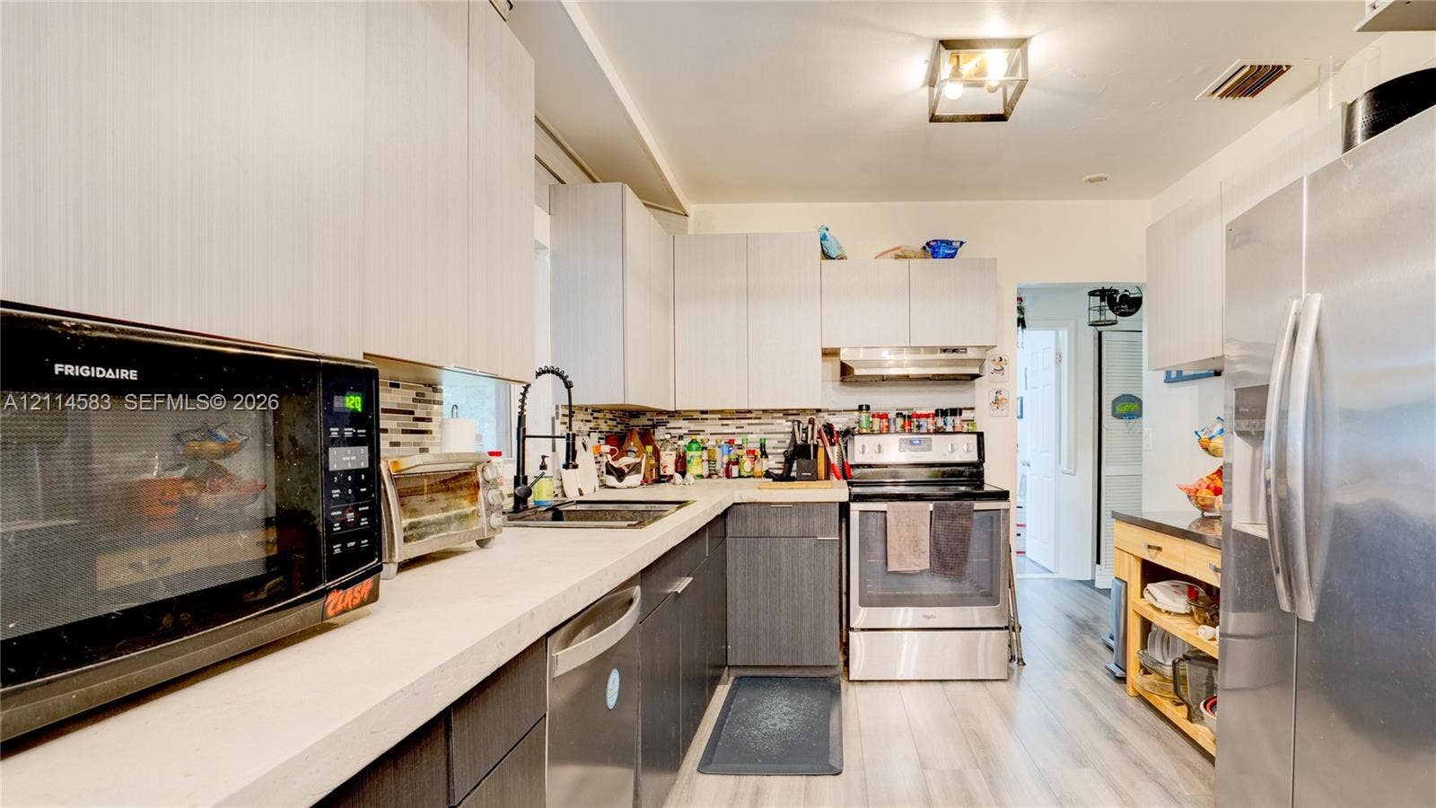 13301 NW Miami Court, Miami, FL 33168 Kitchen featuring flat-panel cabinetry, light-toned countertops, multi-material tile backsplash, stainless steel appliances, and wood-finish flooring