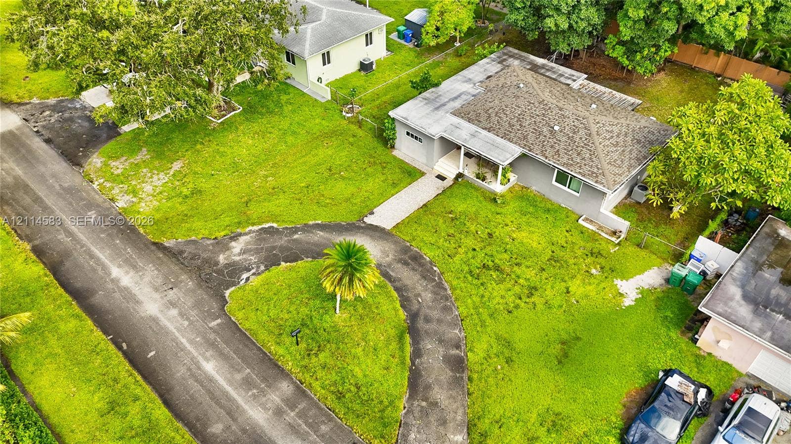 13301 NW Miami Court, Miami, FL 33168 Aerial perspective featuring a single-story residence with a pitched shingle roof, a curved asphalt driveway, and expansive lawn space