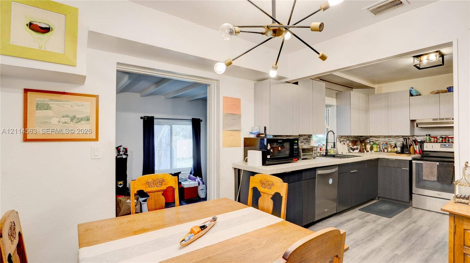 13301 NW Miami Court, Miami, FL 33168 Kitchen featuring two-tone cabinetry, wood-finish flooring, a multi-arm Sputnik-style chandelier, and light-toned solid surface countertops