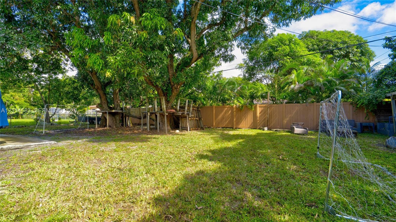 13301 NW Miami Court, Miami, FL 33168 Expansive backyard featuring mature tree canopy, integrated wooden platform structure, and solid perimeter fencing