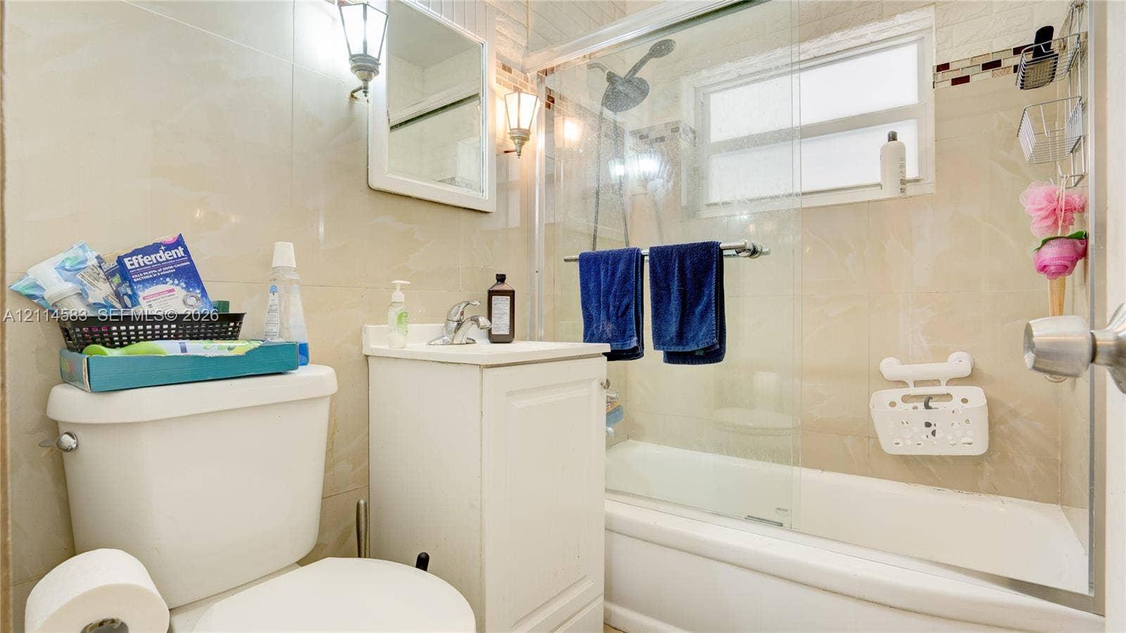 13301 NW Miami Court, Miami, FL 33168 Bathroom featuring floor-to-ceiling neutral wall tile, white vanity cabinet with a chrome faucet, and a shower-tub combination enclosed by a glass panel door