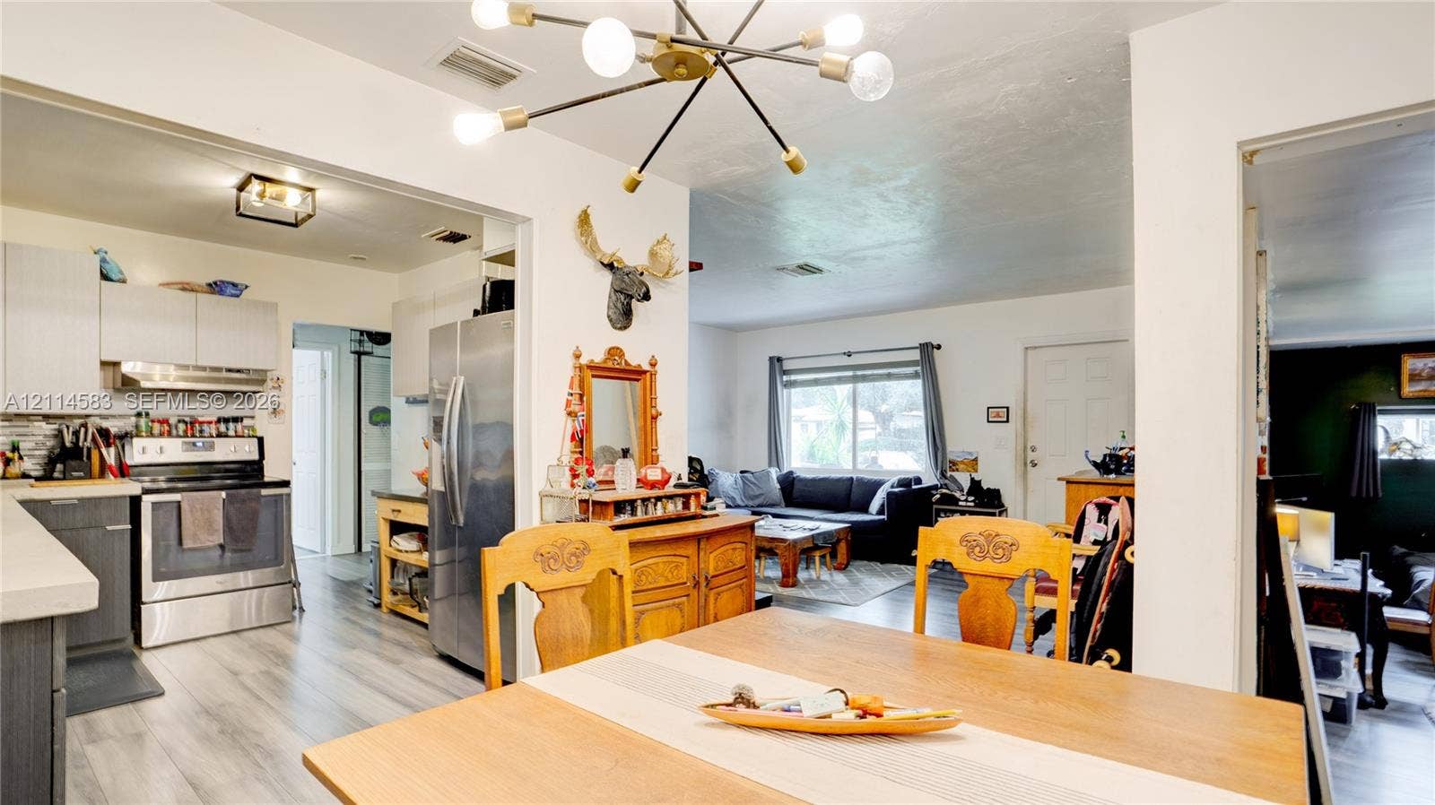 13301 NW Miami Court, Miami, FL 33168 Kitchen featuring stainless steel appliances, flat-panel cabinetry, and light-toned wood-finish flooring, illuminated by a multi-arm modern sputnik chandelier
