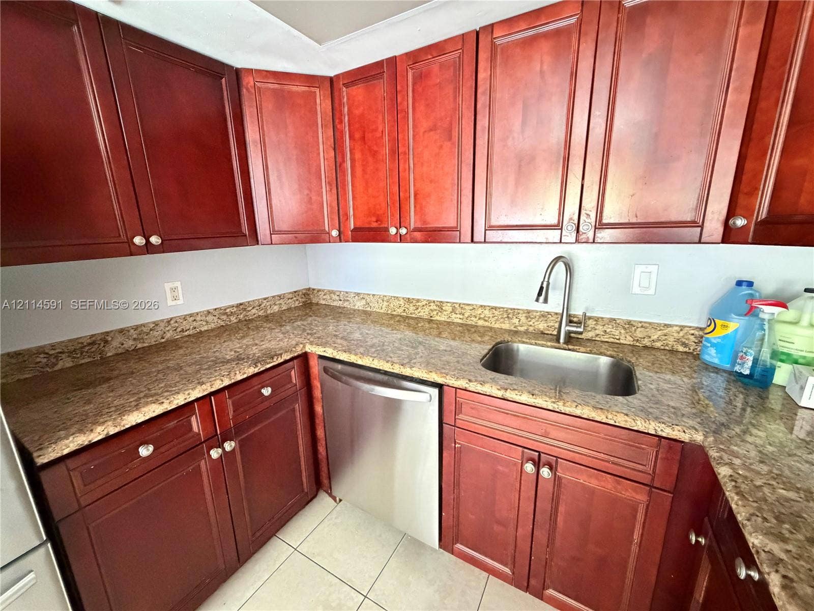 Kitchen featuring stained wood cabinetry, stone-finish countertops, stainless steel undermount sink with a gooseneck faucet, stainless steel dishwasher, and ceramic tile flooring