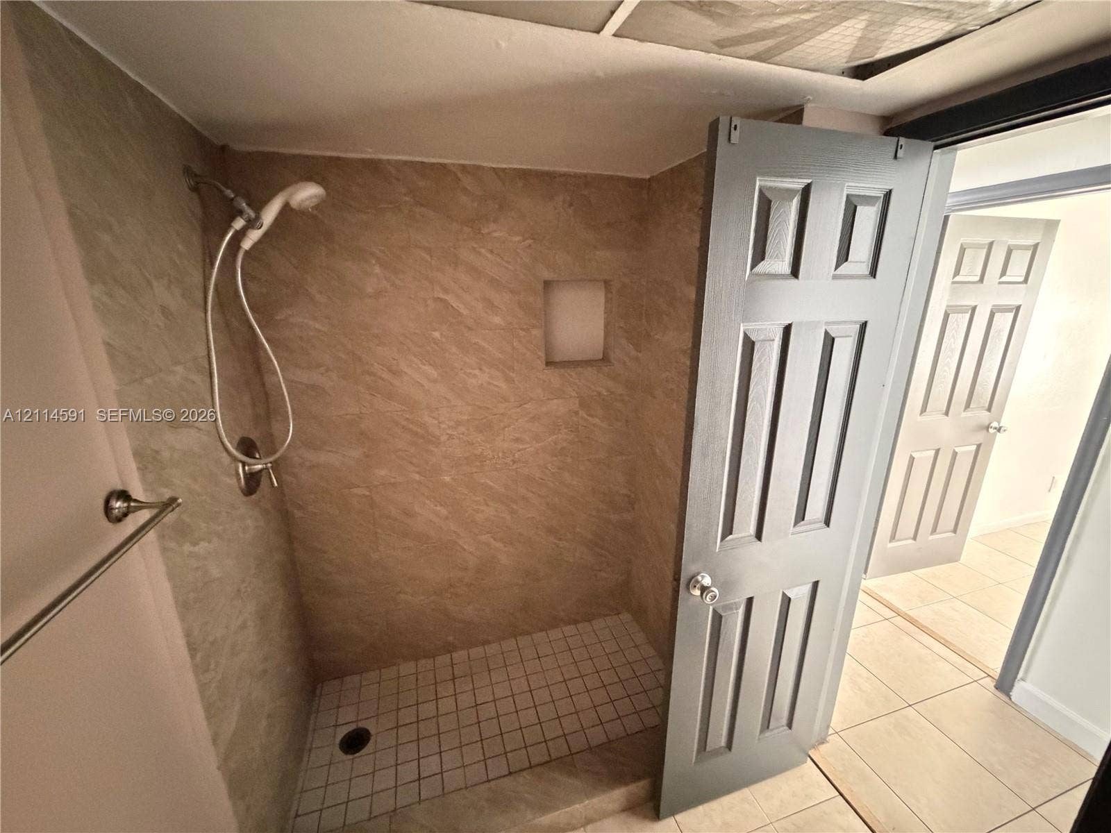 Shower stall featuring beige stone-finish tile surround, integrated wall niche, handheld showerhead, and mosaic tile flooring