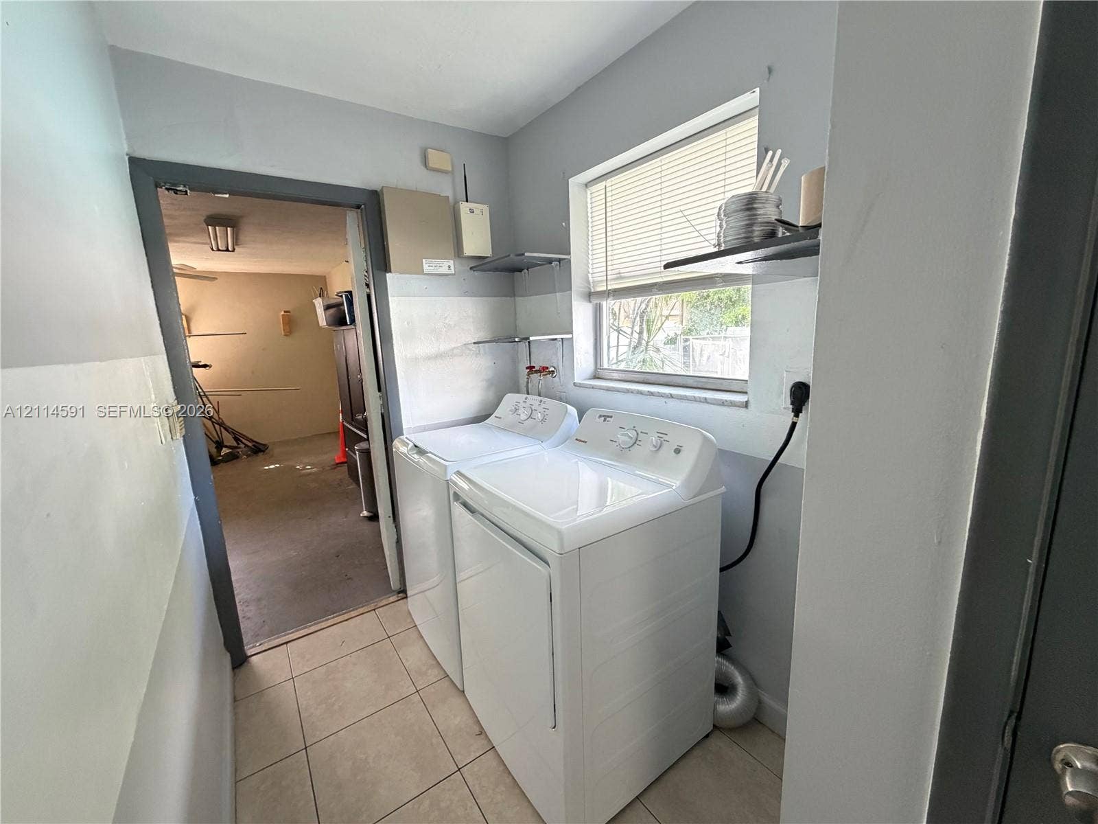Laundry area featuring tile flooring, a window, and wall-mounted shelving