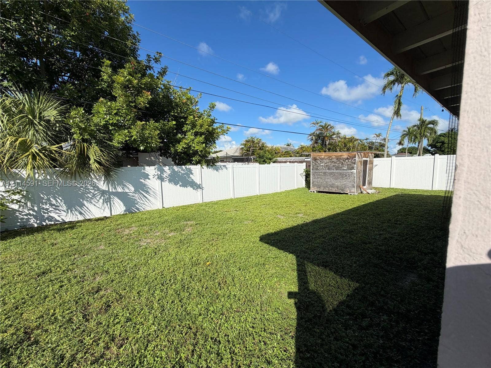 Backyard featuring a grass lawn, white vinyl fencing, and mature trees