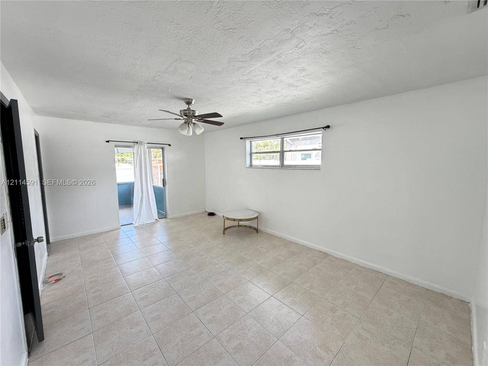 Interior room featuring large-format ceramic tile flooring, a multi-blade ceiling fan with integrated lighting, a rectangular single-hung window, and a sliding glass door