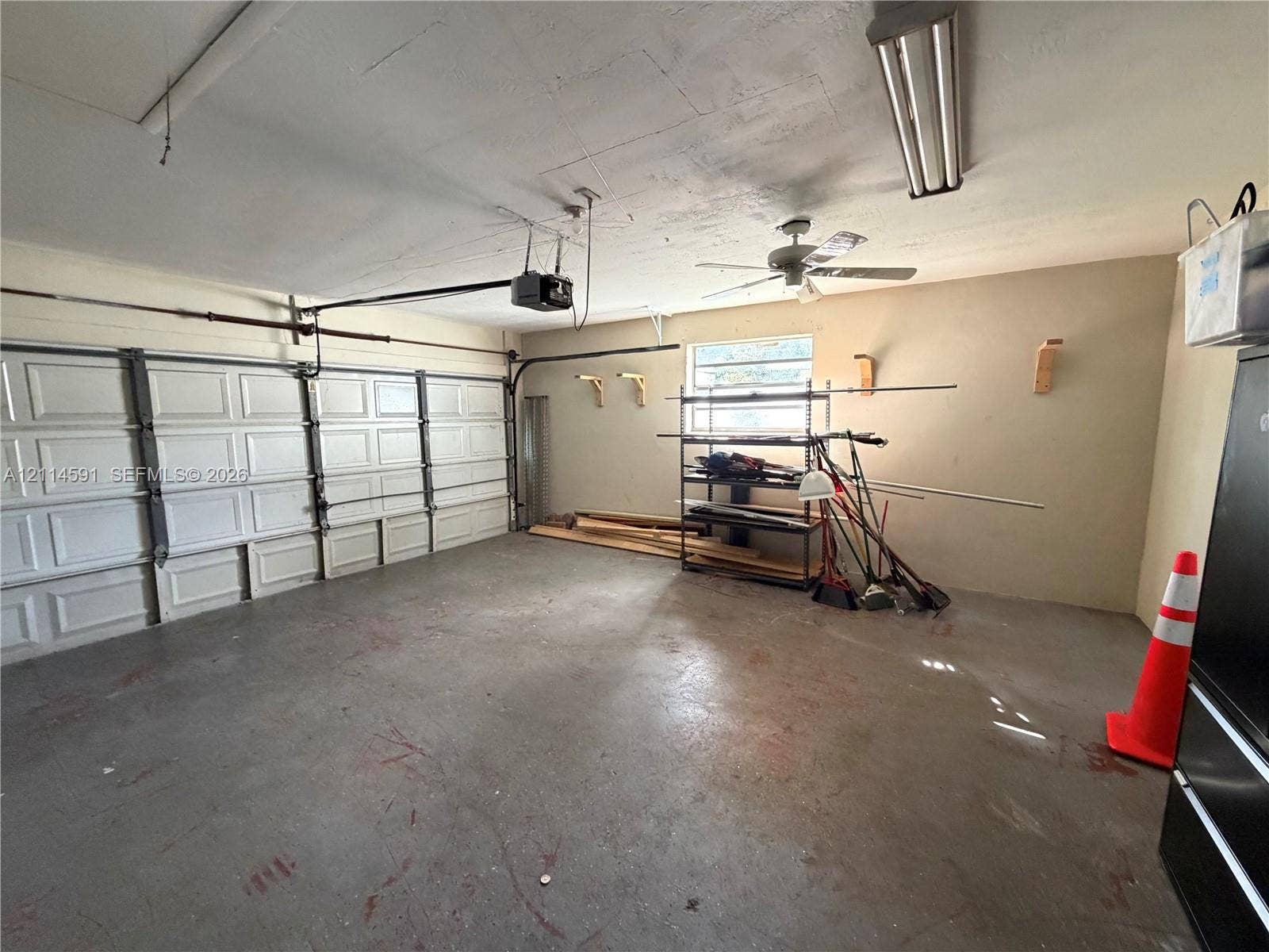 Two-car garage featuring a segmented overhead door, ceiling-mounted paddle fan, integrated fluorescent lighting, and a single-pane window