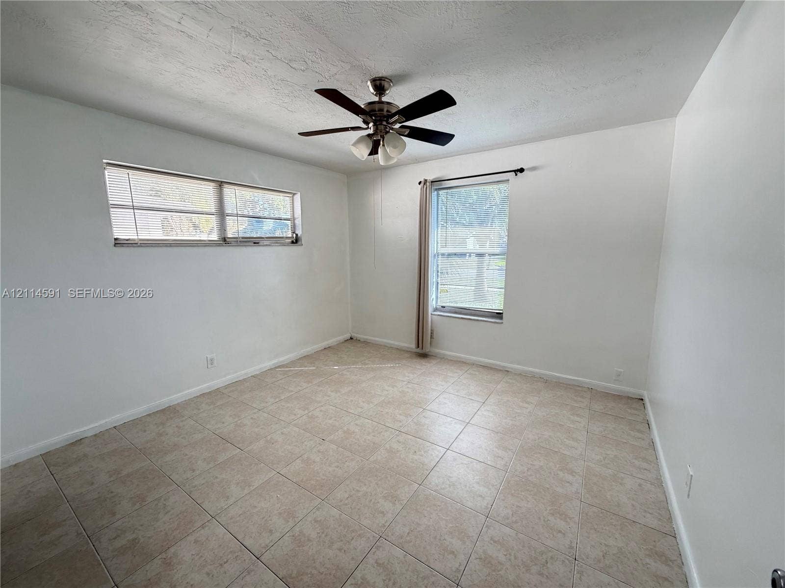 Neutral interior room featuring tile flooring, dual-pane windows, and a central ceiling fan with integrated lighting