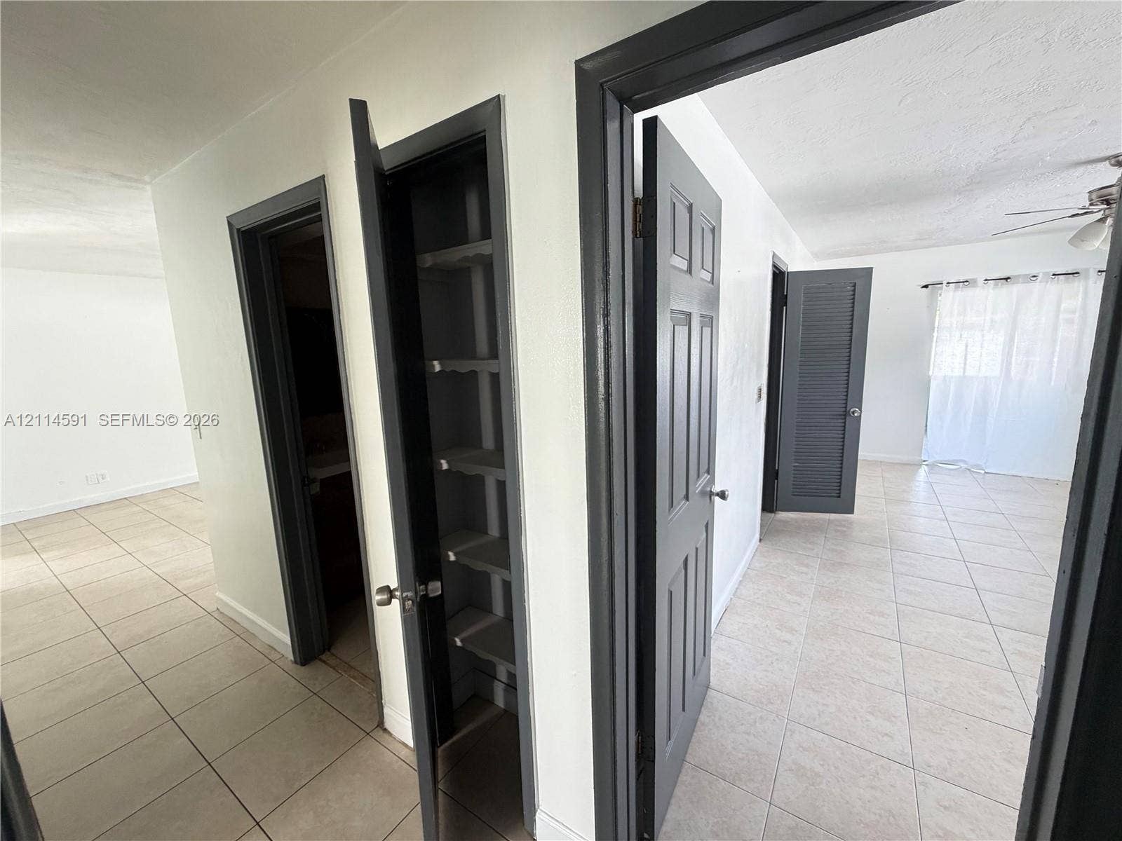Hallway featuring neutral-toned tile flooring, built-in shelving, six-panel interior doors, and louvered closet doors with contrasting dark trim