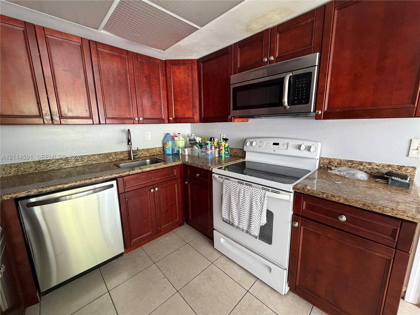Kitchen featuring warm-tone wooden cabinetry, stone-finish countertops, stainless steel dishwasher, integrated over-the-range microwave, and tile flooring