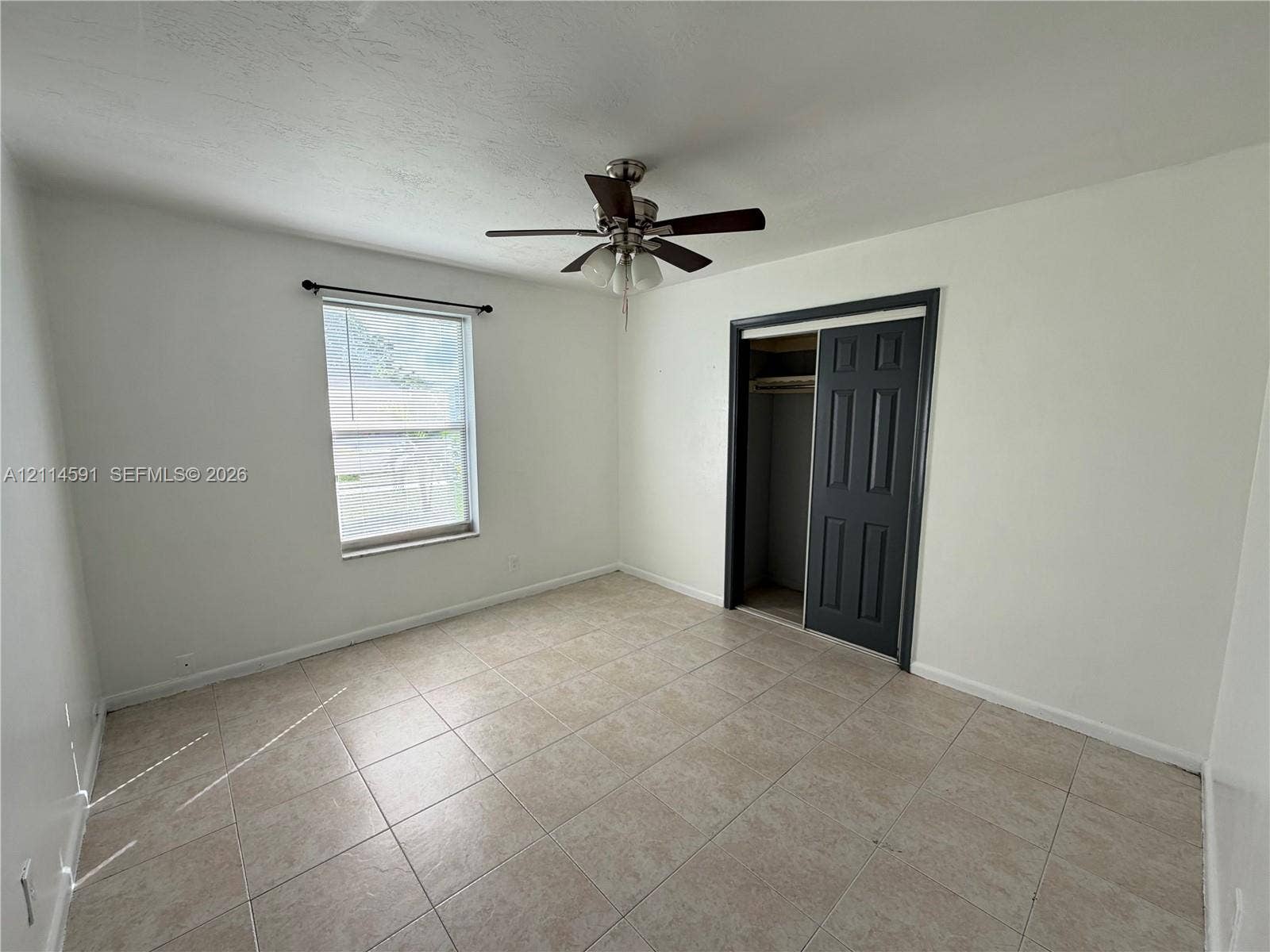 Neutral-toned tiled flooring, ceiling fan with integrated lighting, single-pane window, and a closet with dark-finished paneled doors
