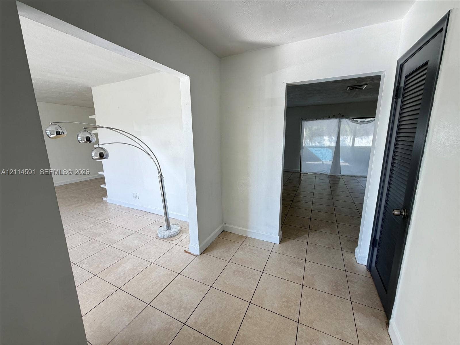 Interior space featuring neutral tile flooring, stark white walls, and a black louvered door