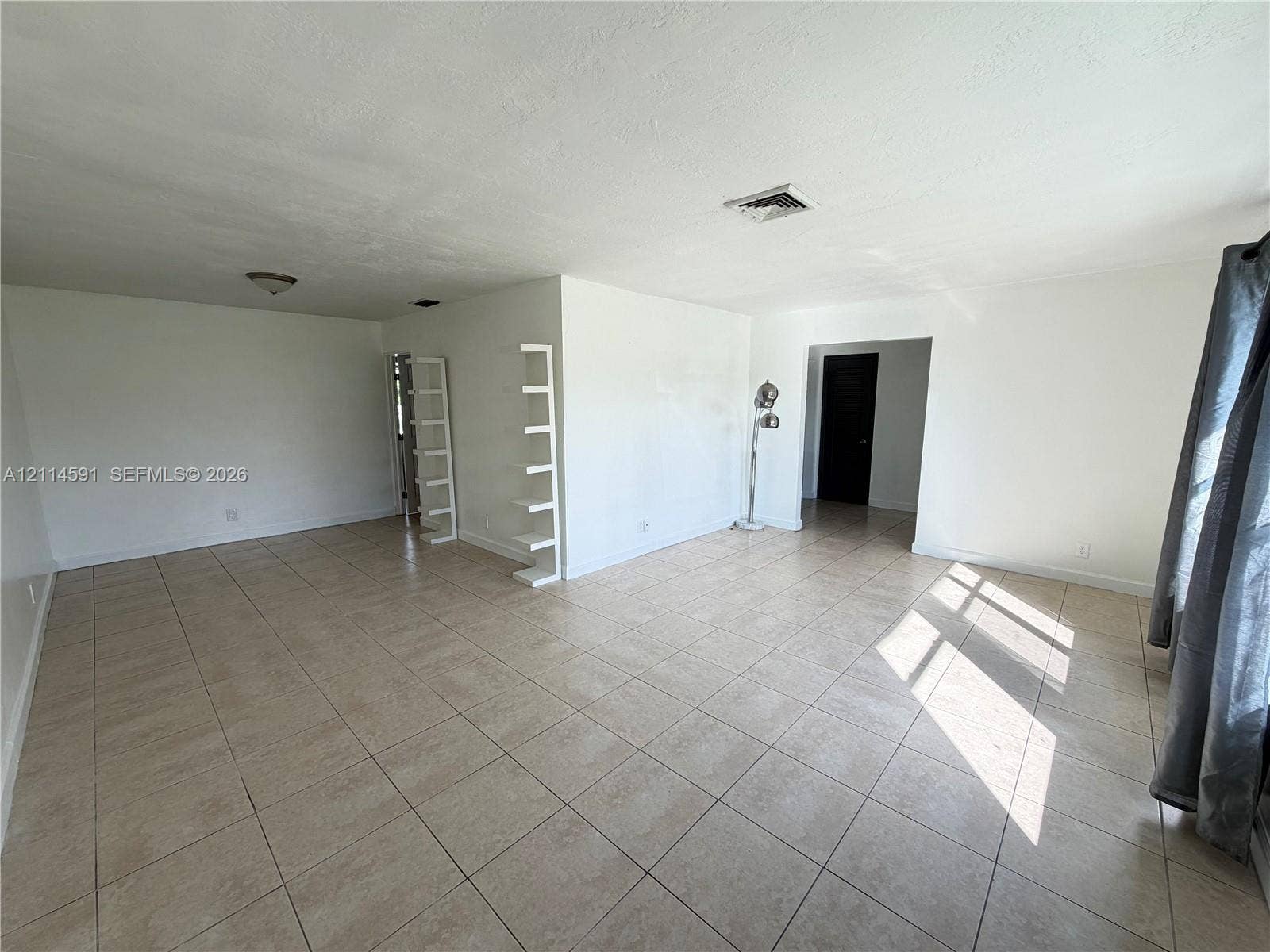 Spacious interior featuring neutral ceramic tile flooring, bright white walls, and built-in wall shelving