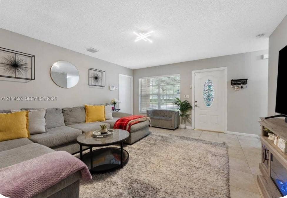 12230 Dartmoor Drive, Wellington, FL 33414 Neutral wall tones featuring tile flooring, multi-pane window, and decorative entry door with an oval glass insert, illuminated by a contemporary geometric light fixture