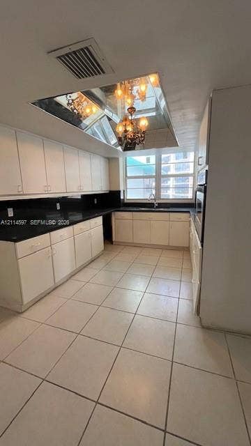5255 Collins Avenue, #5J, Miami Beach, Miami Beach, FL 33140 Kitchen featuring white cabinetry, dark countertops, tile flooring, an integrated wall oven, and a mirrored ceiling fixture with a hanging chandelier