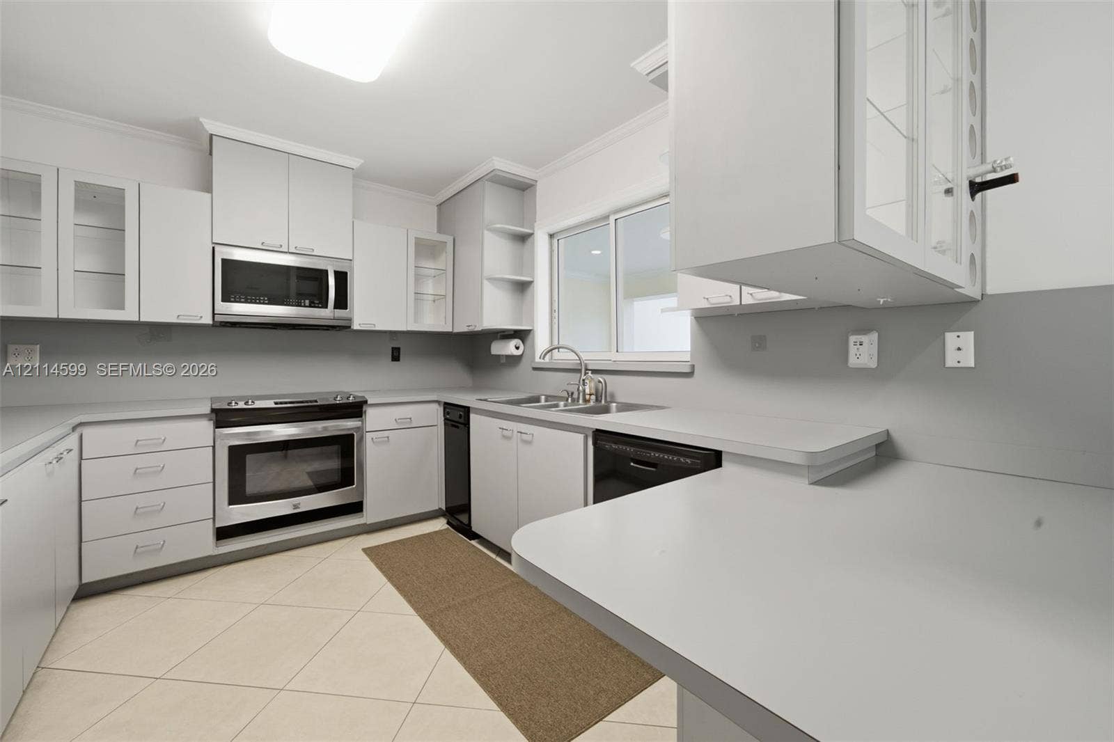 Kitchen featuring light grey cabinetry, stainless steel appliances, solid surface countertops, a double-basin stainless steel sink, and large-format tile flooring