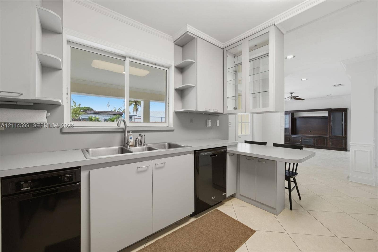 Kitchen featuring light grey cabinetry, glass-front upper cabinets, integrated countertop seating, double-basin stainless steel sink, and black appliances