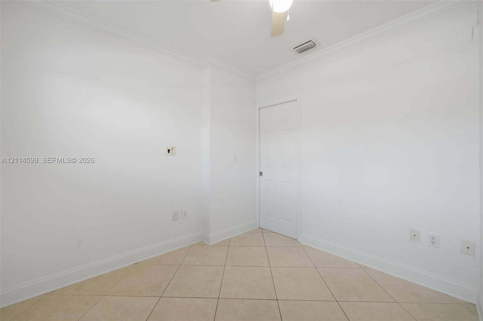 Interior room featuring neutral ceramic tile flooring, crown molding, a six-panel door, and a ceiling-mounted light fixture