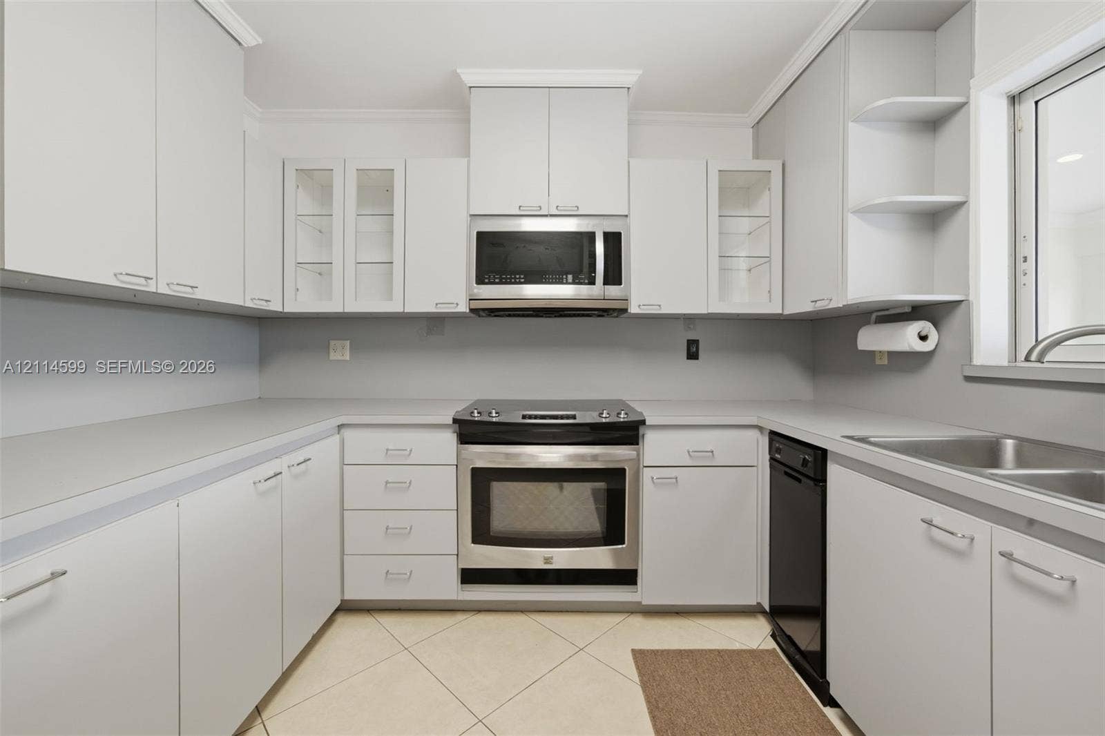Kitchen featuring light-toned cabinetry with glass-front display panels, stainless steel appliances, open shelving, a double-basin stainless steel sink, and tile flooring