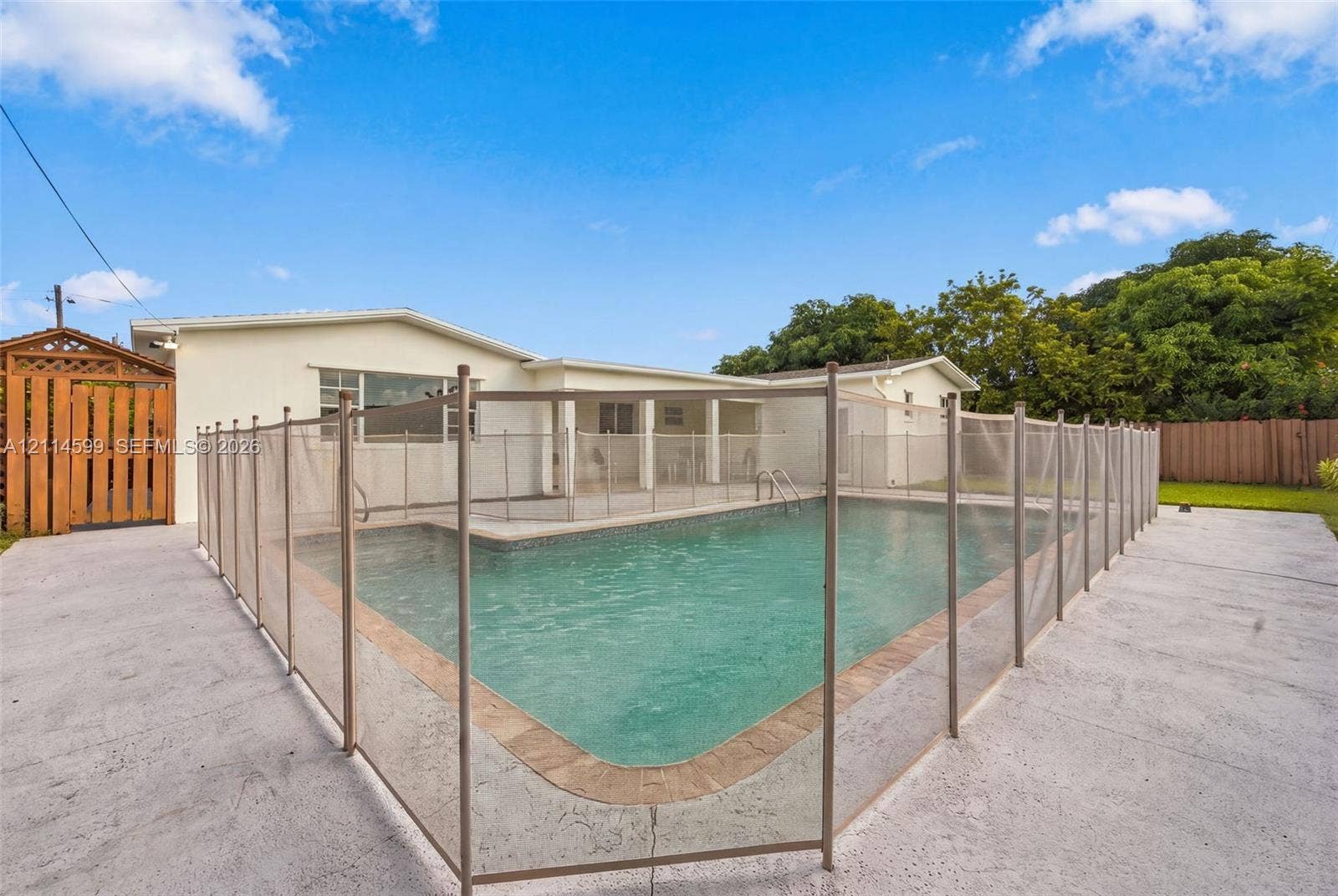 In-ground swimming pool featuring a concrete deck, perimeter safety fencing, and an attached covered patio