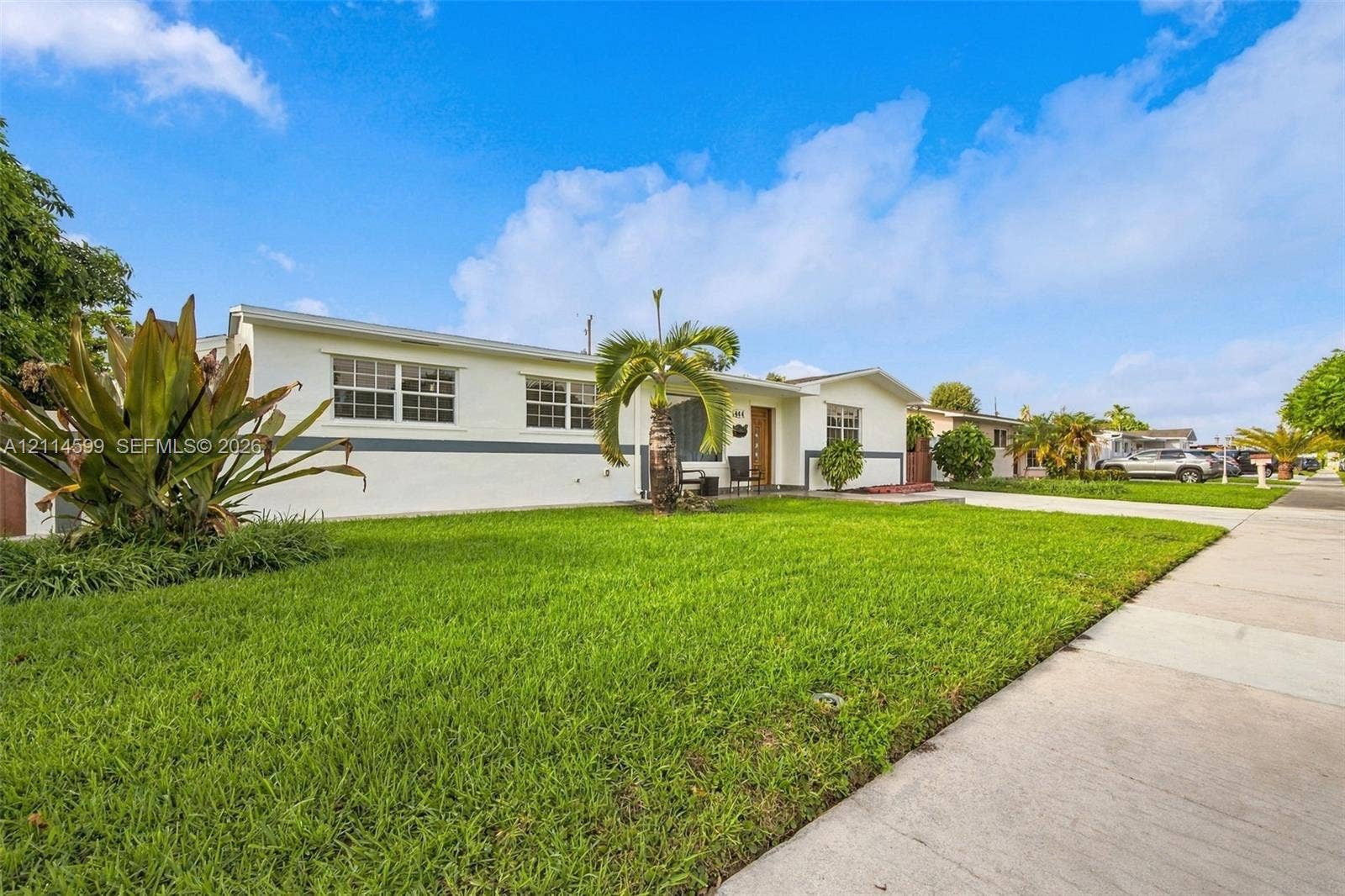 Single-story residence featuring a smooth stucco exterior, manicured front lawn, palm tree landscaping, and a concrete driveway