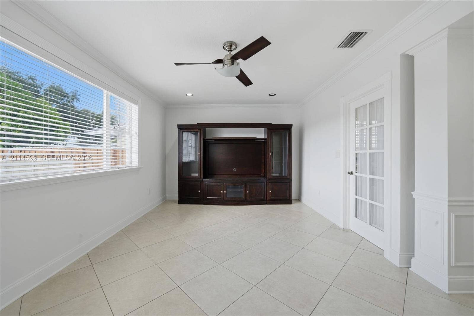 Interior space featuring large-format tile flooring, crown molding, built-in dark wood cabinetry, a ceiling fan, and a glass-paneled door