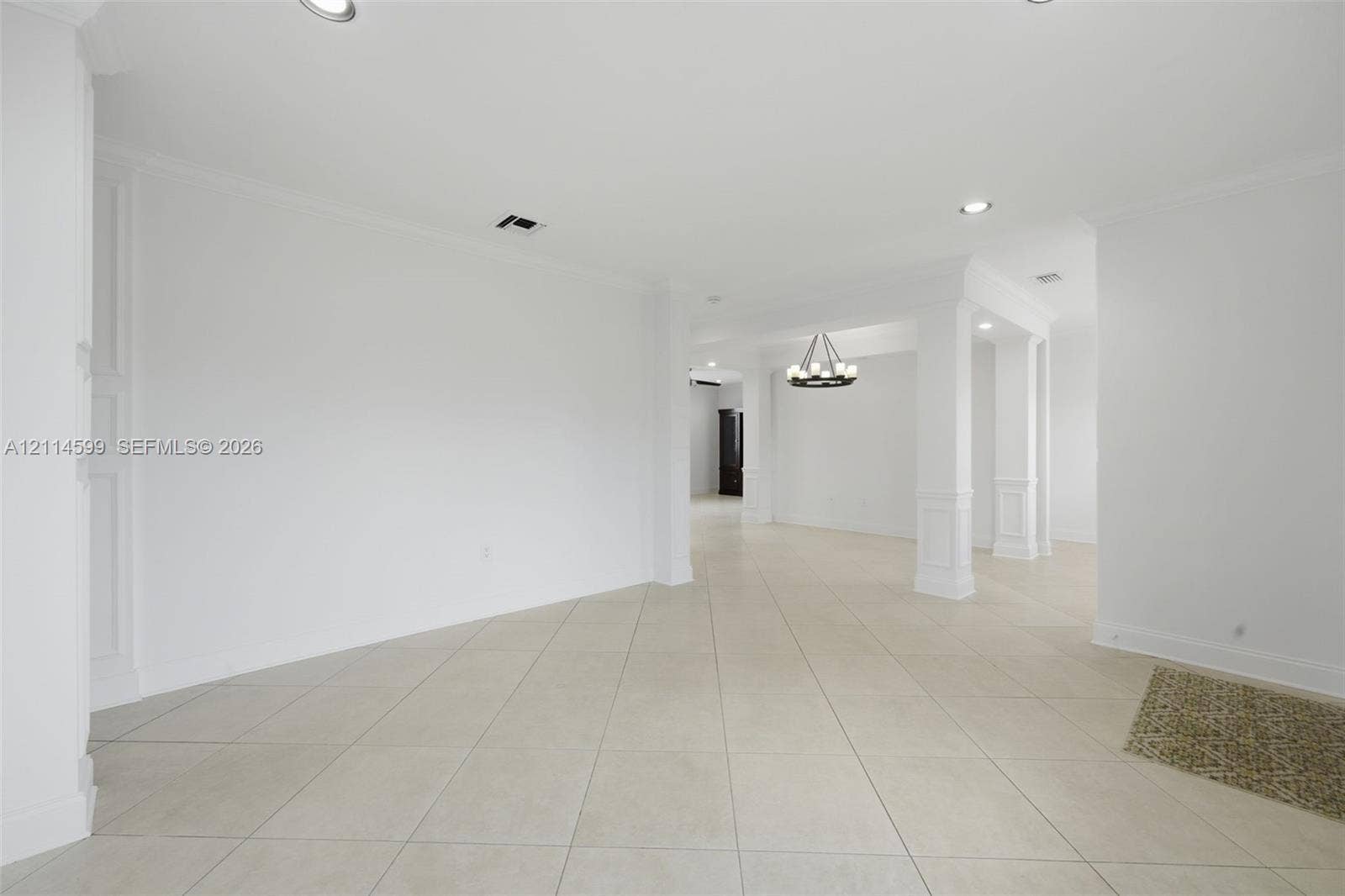 Open floor plan featuring large-format ceramic tile flooring, recessed lighting, architectural columns with wainscoting detail, and a multi-light chandelier