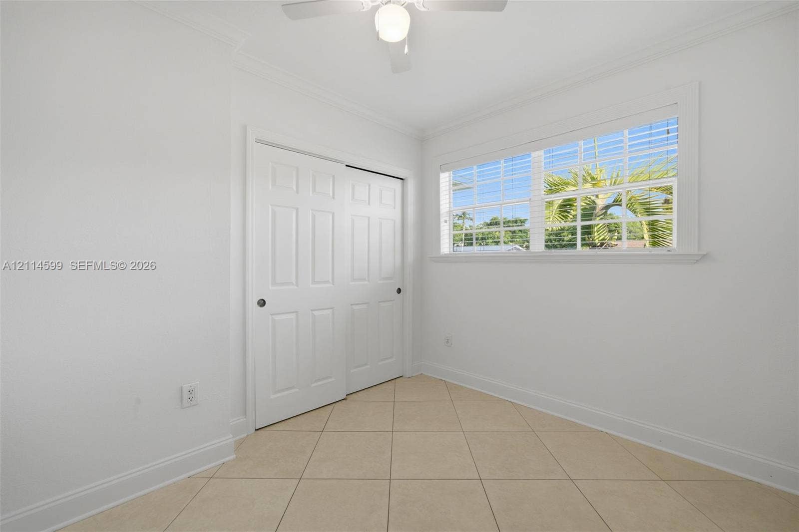 Neutral-toned tile flooring, white six-panel closet doors, single-hung window with muntins, and a ceiling-mounted fan