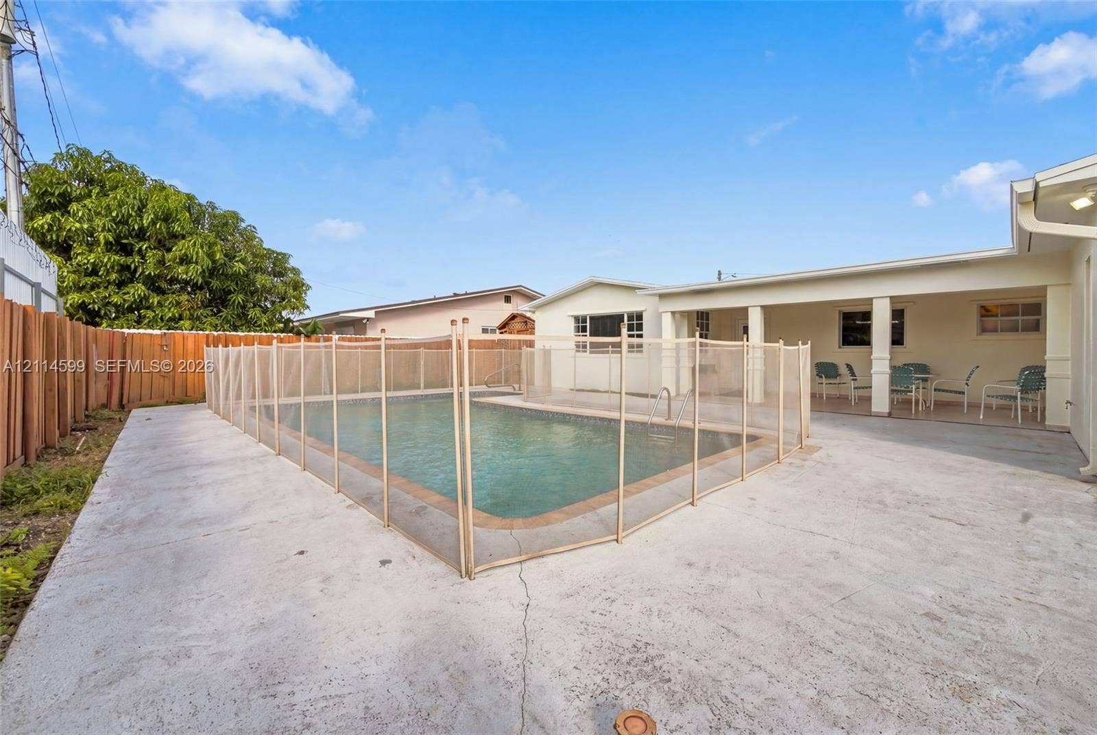 Backyard featuring an in-ground pool with mesh safety fencing, covered patio, concrete deck, and perimeter wood fencing