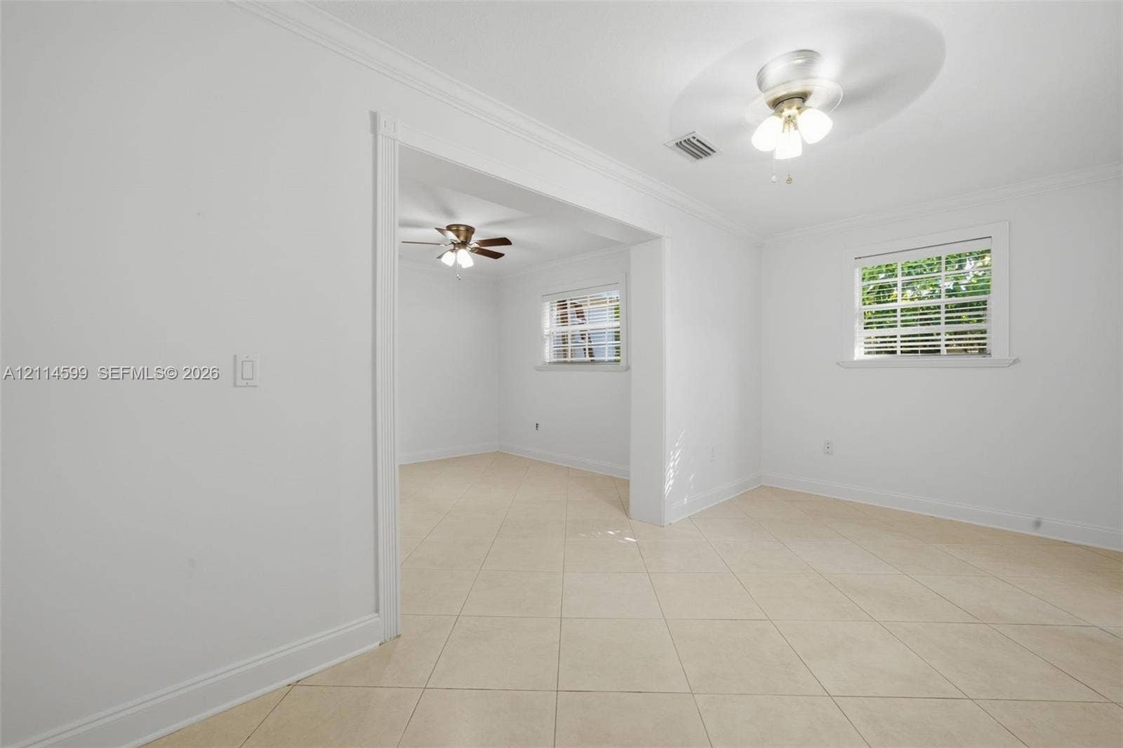 Neutral-toned tile flooring, crown molding, and two ceiling-mounted light fixtures with integrated fans