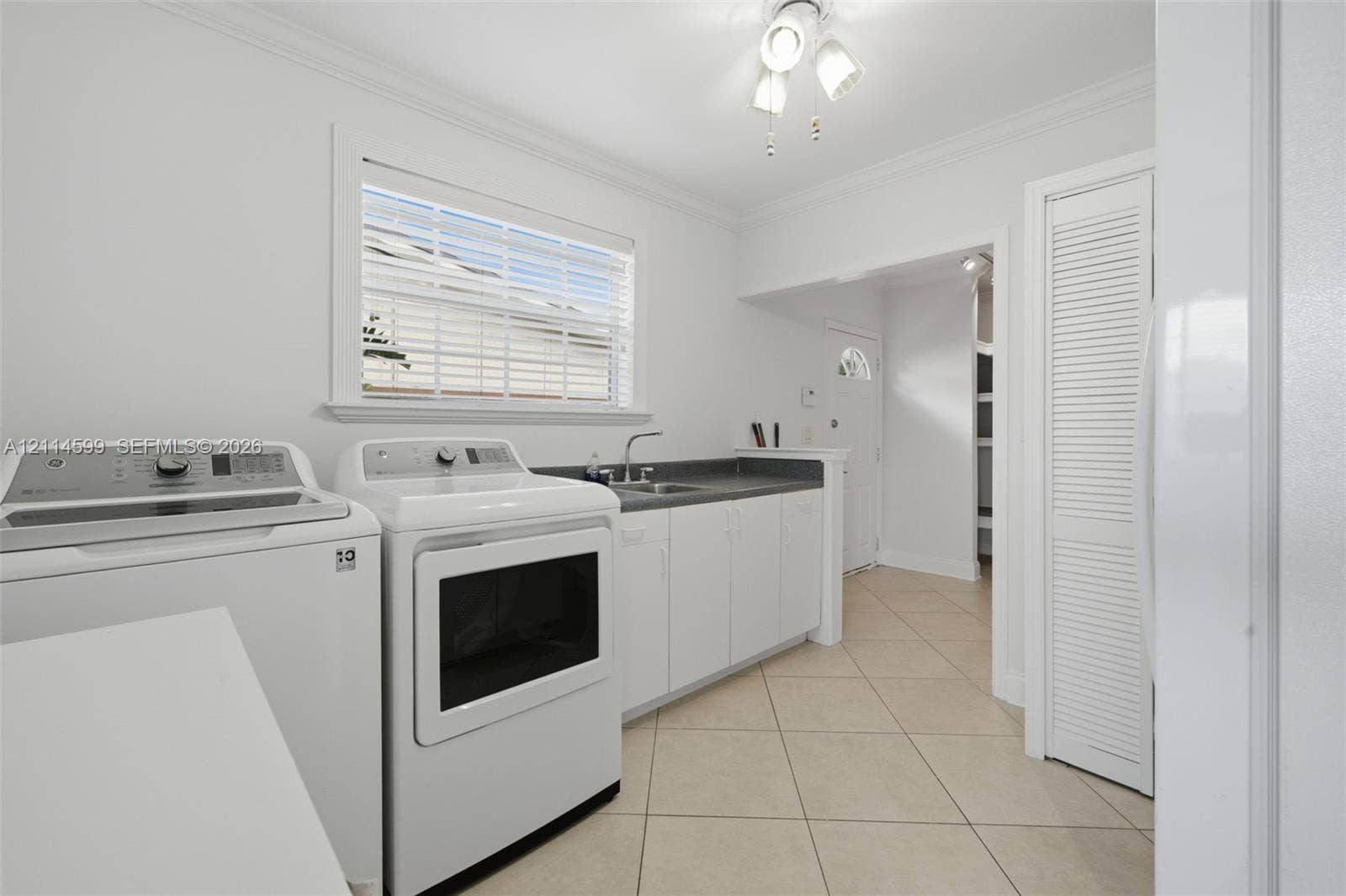 Utility area featuring tile flooring, white cabinetry, a countertop with a built-in sink, and louvered closet doors