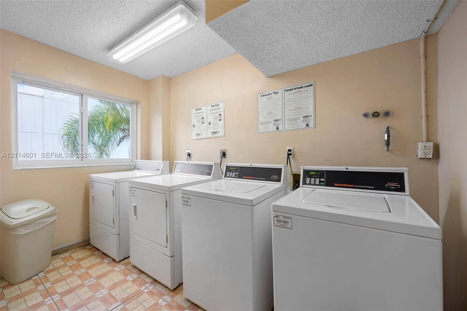 6801 Harding Avenue, #311, Miami Beach, Miami Beach, FL 33141 Laundry room featuring multiple high-capacity washer and dryer units, a large window, fluorescent overhead lighting, and durable tiled flooring