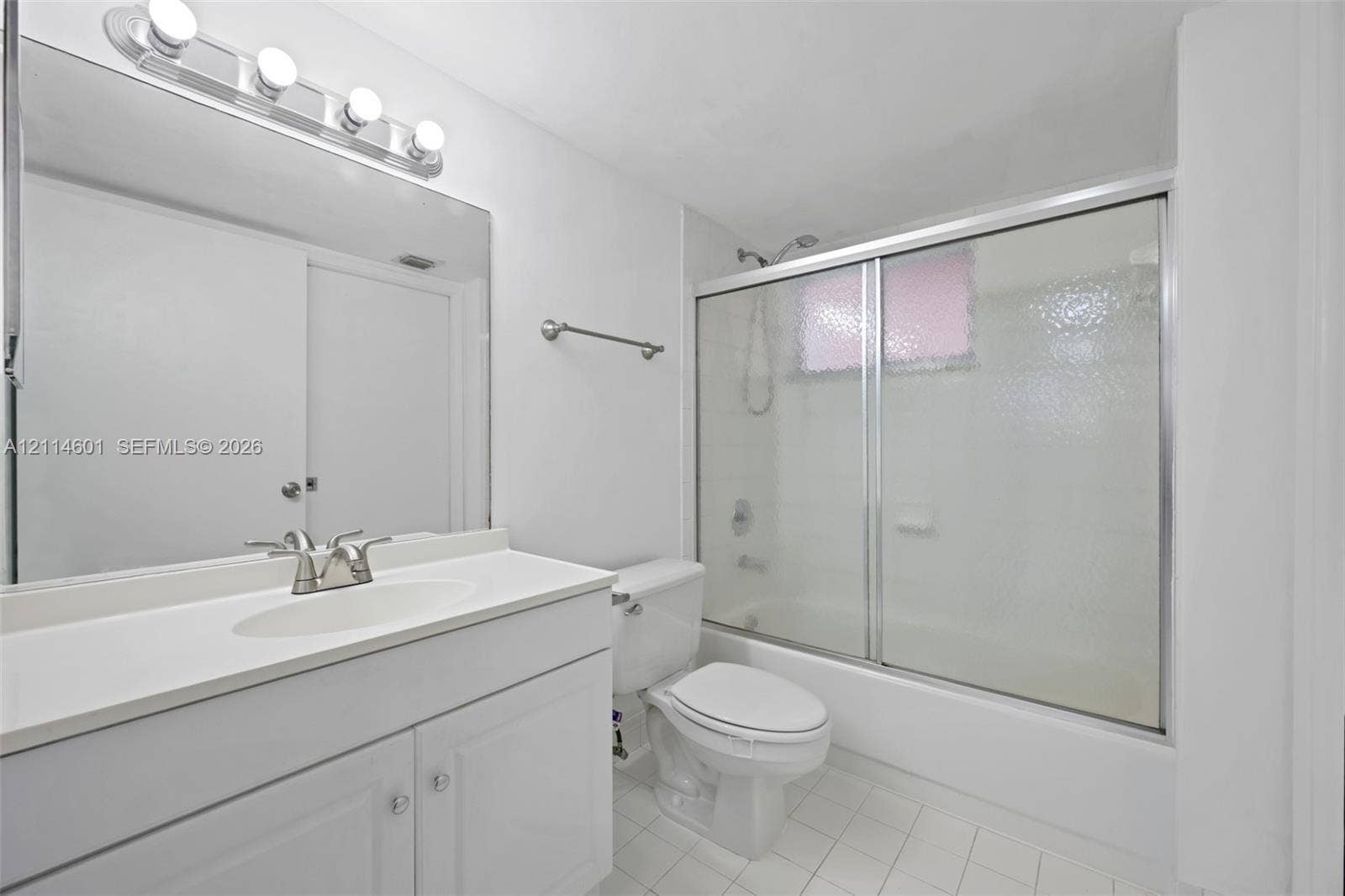 6801 Harding Avenue, #311, Miami Beach, Miami Beach, FL 33141 Bathroom featuring a white vanity with an integrated sink, full-width wall mirror, four-bulb vanity lighting fixture, and a tub-shower combination enclosed by textured glass sliding doors