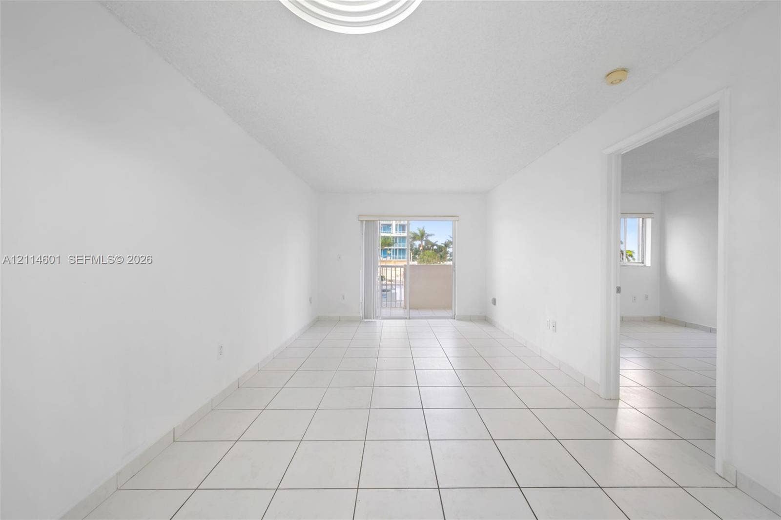 6801 Harding Avenue, #311, Miami Beach, Miami Beach, FL 33141 Interior space featuring white ceramic tile flooring, neutral wall finishes, and glass sliding doors leading to an exterior balcony
