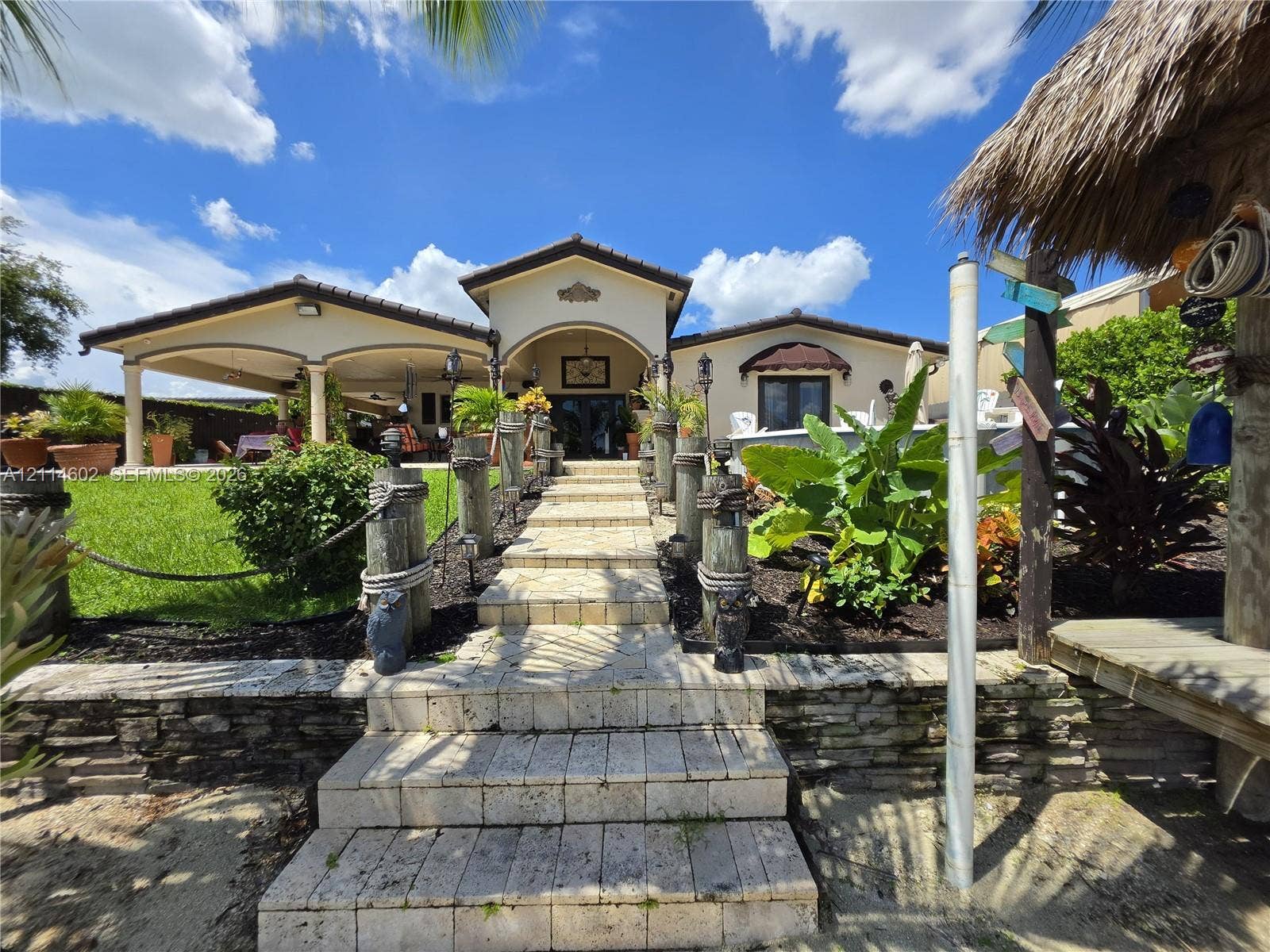 8450 NW 178th Street, Hialeah, Hialeah, FL 33015 Stone walkway with wood pilings and rope railing, covered patio with arched supports, and tiered stone retaining wall