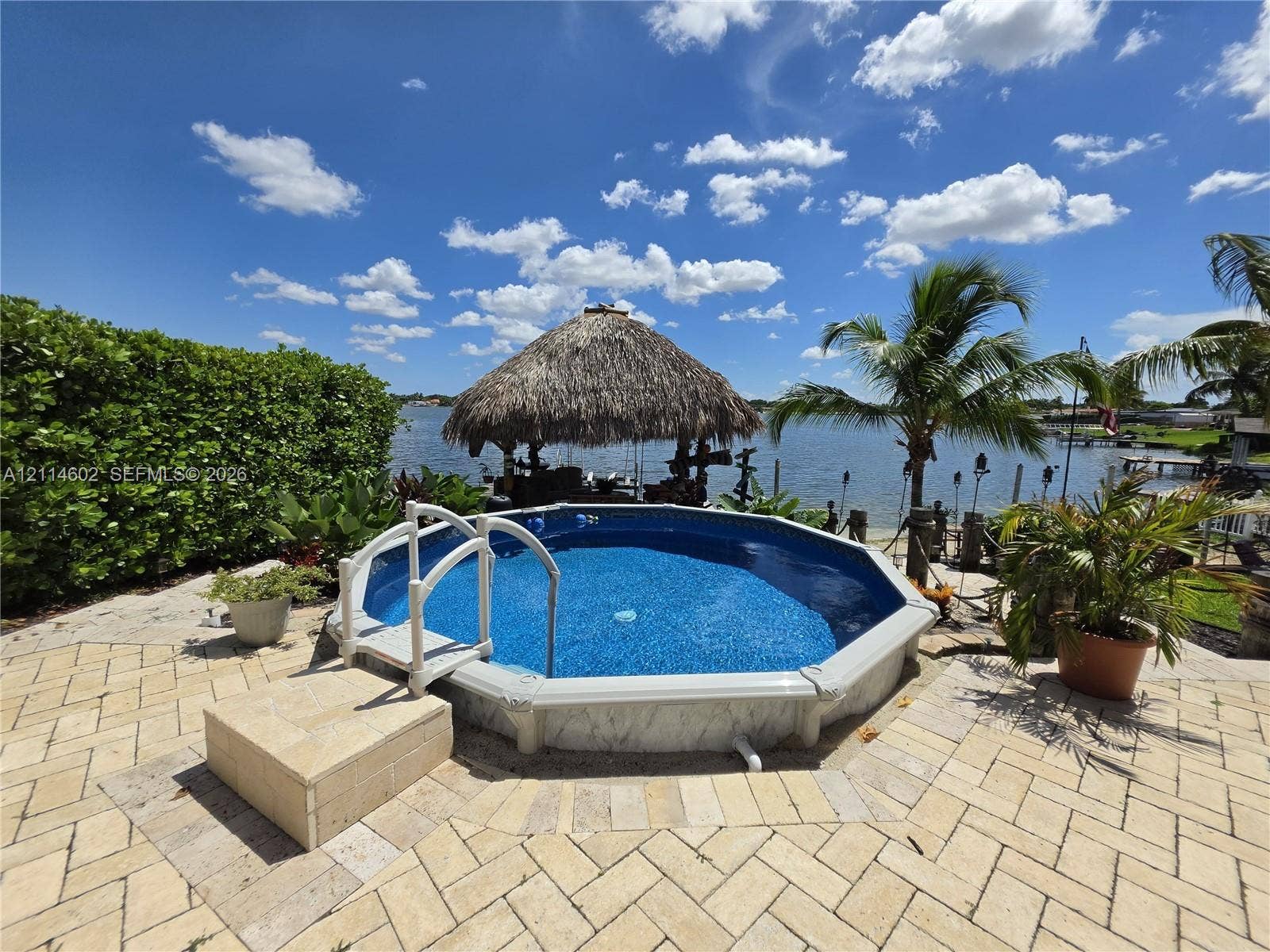 8450 NW 178th Street, Hialeah, Hialeah, FL 33015 Above-ground pool with a surrounding paved patio, thatched-roof cabana, and waterfront bulkhead