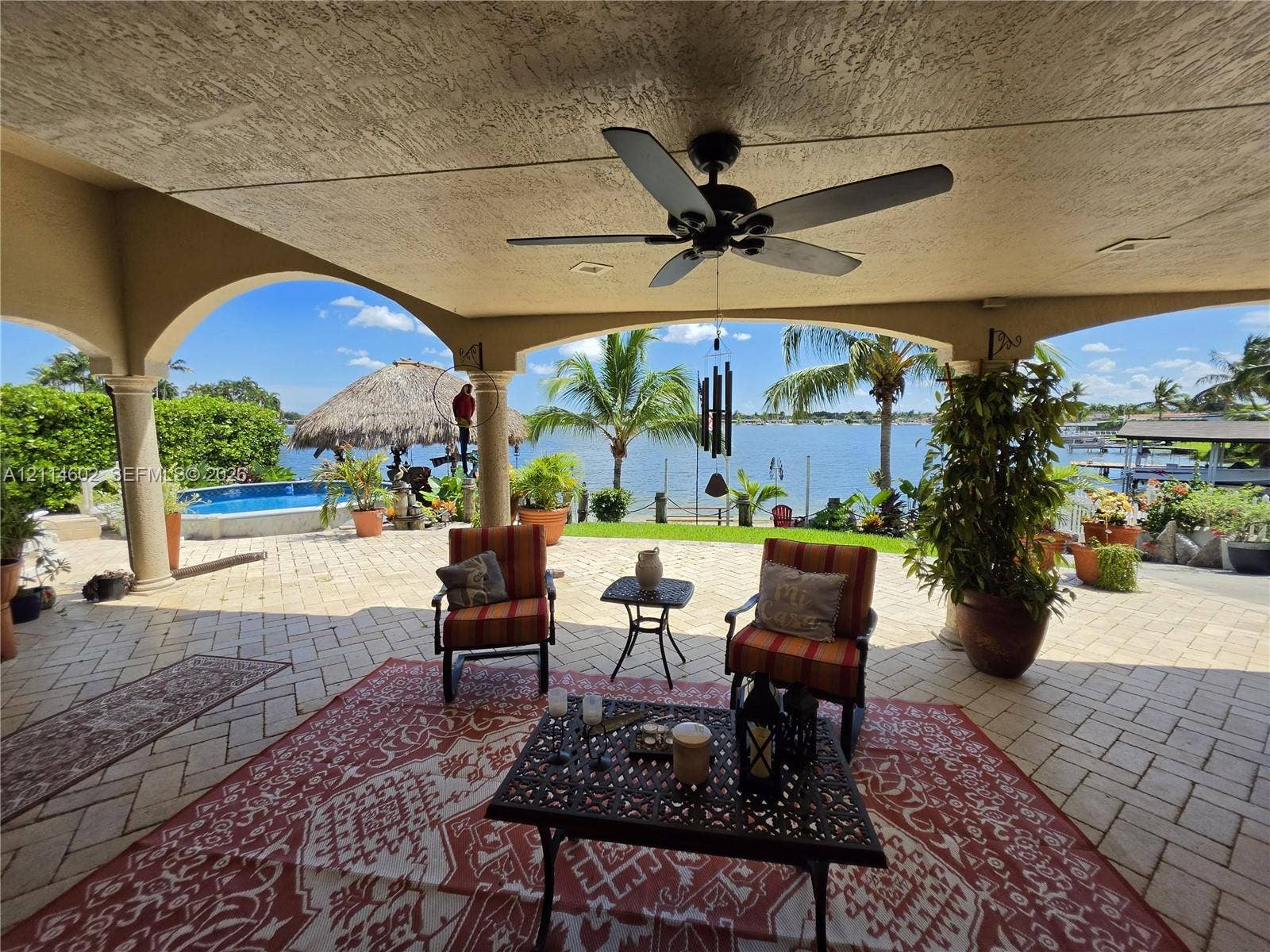 8450 NW 178th Street, Hialeah, Hialeah, FL 33015 Covered lanai featuring arched columns, paved flooring, and a ceiling fan, overlooking a pool and waterfront