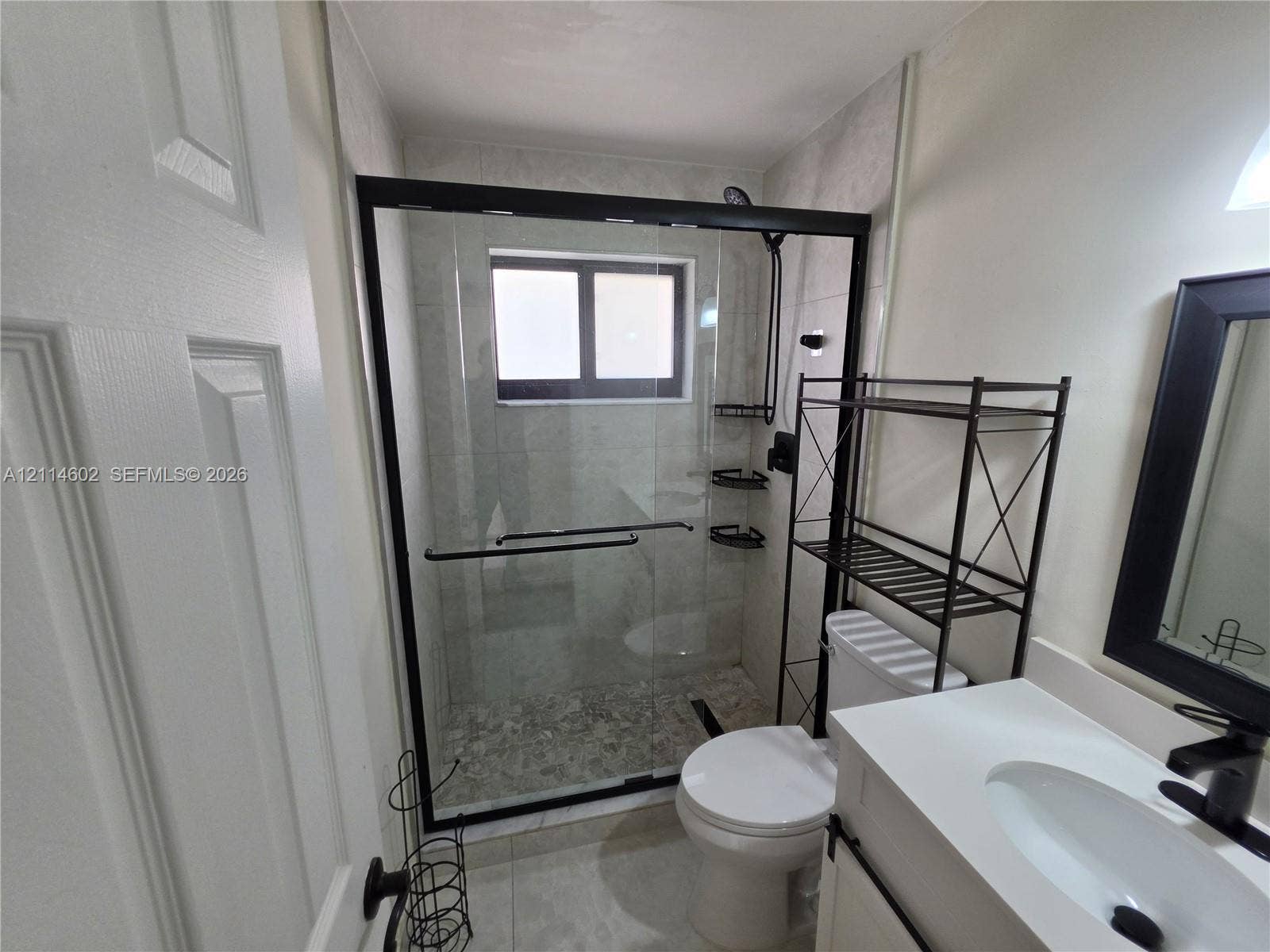 8450 NW 178th Street, Hialeah, Hialeah, FL 33015 Walk-in shower featuring a sliding glass enclosure with a black frame, tiled wall surround, and pebble-finish shower floor