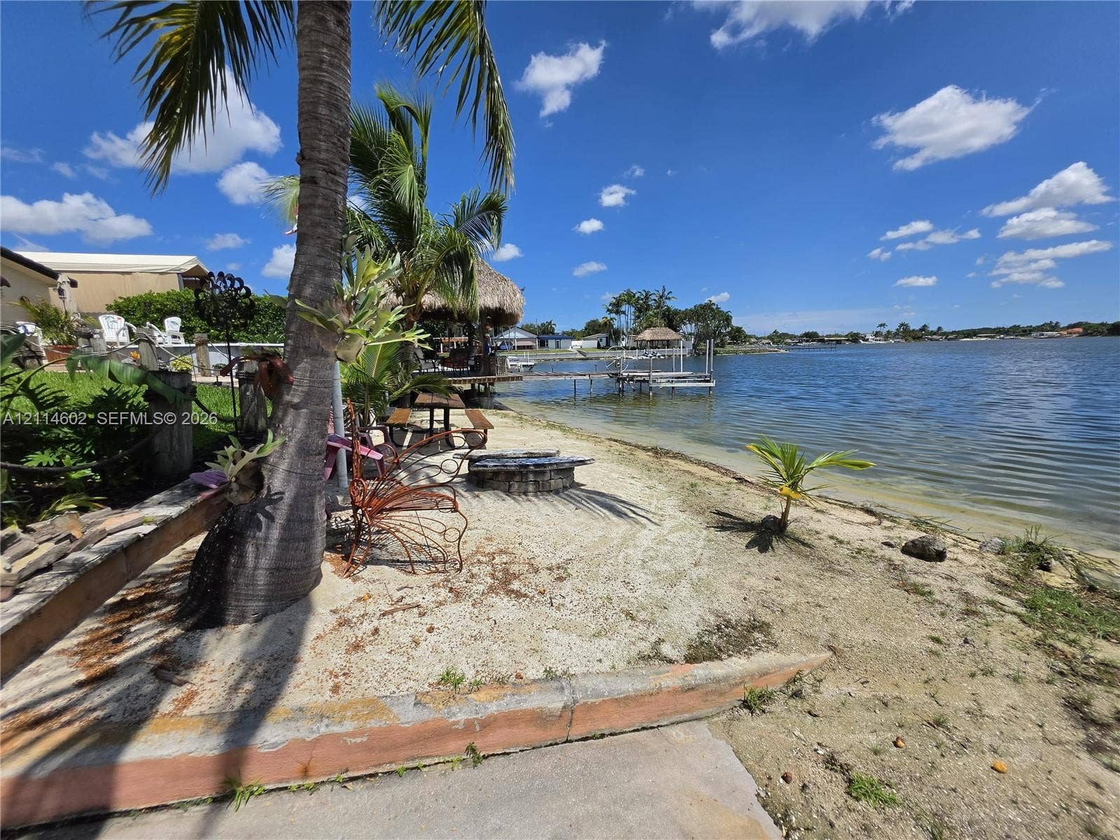 8450 NW 178th Street, Hialeah, Hialeah, FL 33015 Waterfront property featuring a private sandy shoreline, concrete retaining wall, stone fire pit, thatched-roof gazebo, and private dock