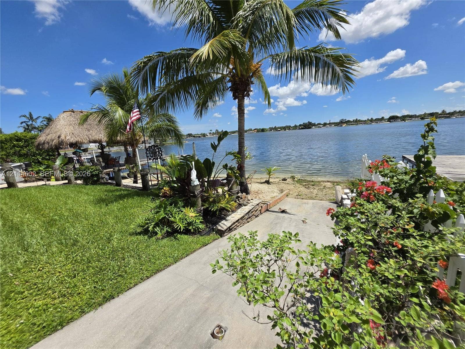 8450 NW 178th Street, Hialeah, Hialeah, FL 33015 Waterfront property featuring a concrete launch, sand shoreline, mature palm trees, tropical landscaping, and a thatched-roof pavilion