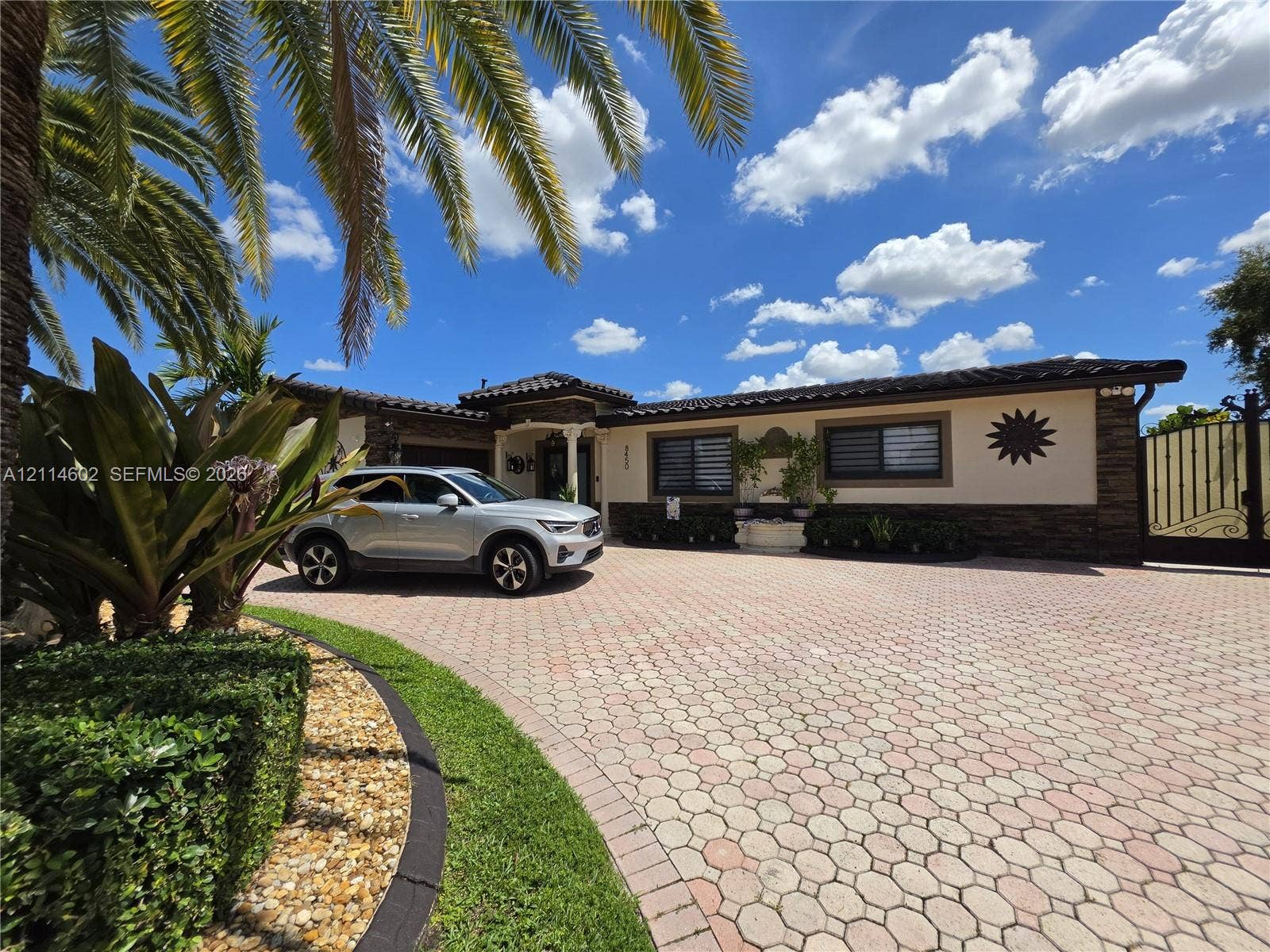 8450 NW 178th Street, Hialeah, Hialeah, FL 33015 Exterior facade featuring stone veneer accents, a paver driveway, an arched entryway with decorative columns, and a custom wrought iron gate