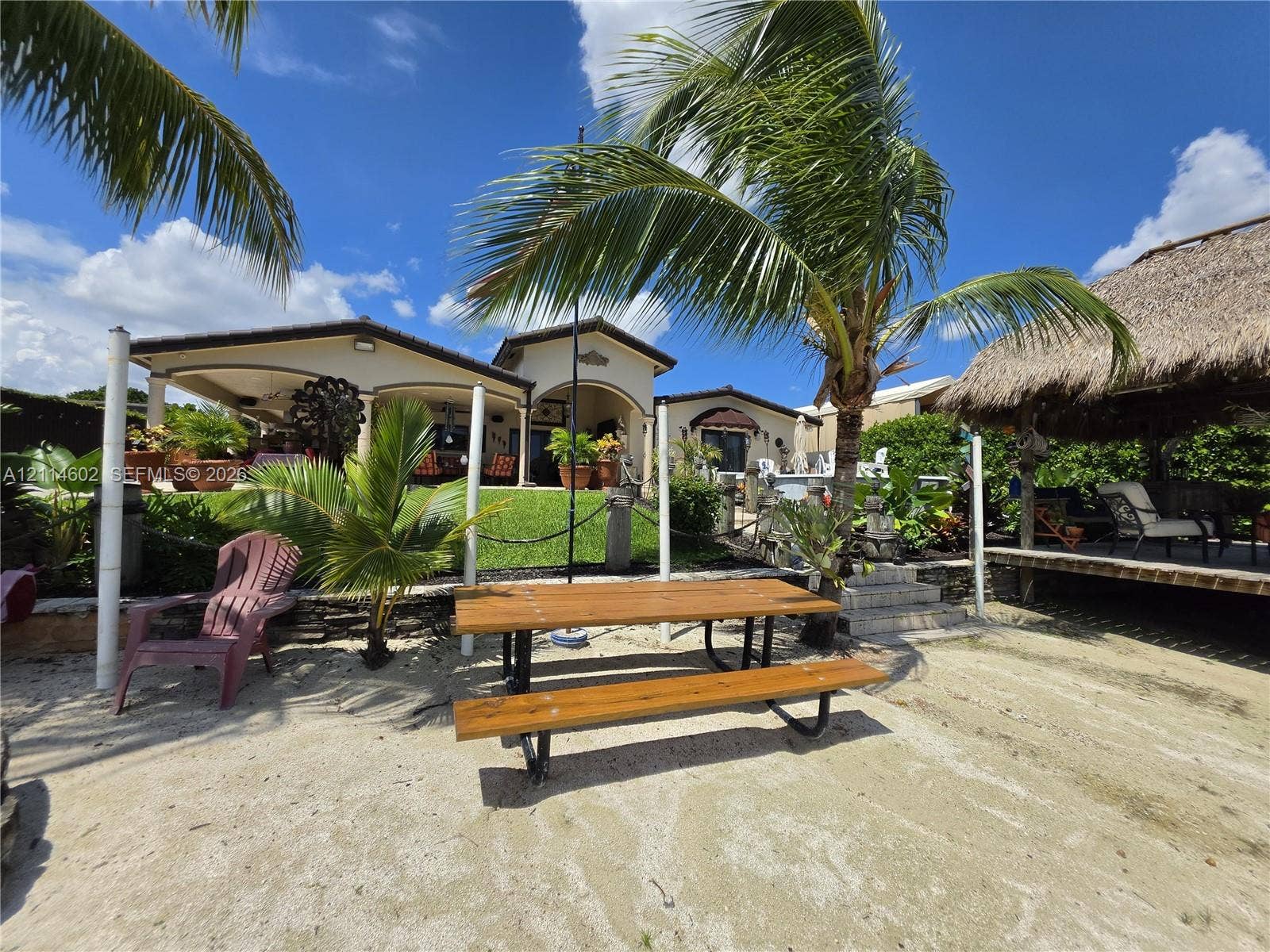8450 NW 178th Street, Hialeah, Hialeah, FL 33015 Outdoor living area featuring a covered patio, a thatched-roof tiki hut, sandy shoreline, and mature palm trees